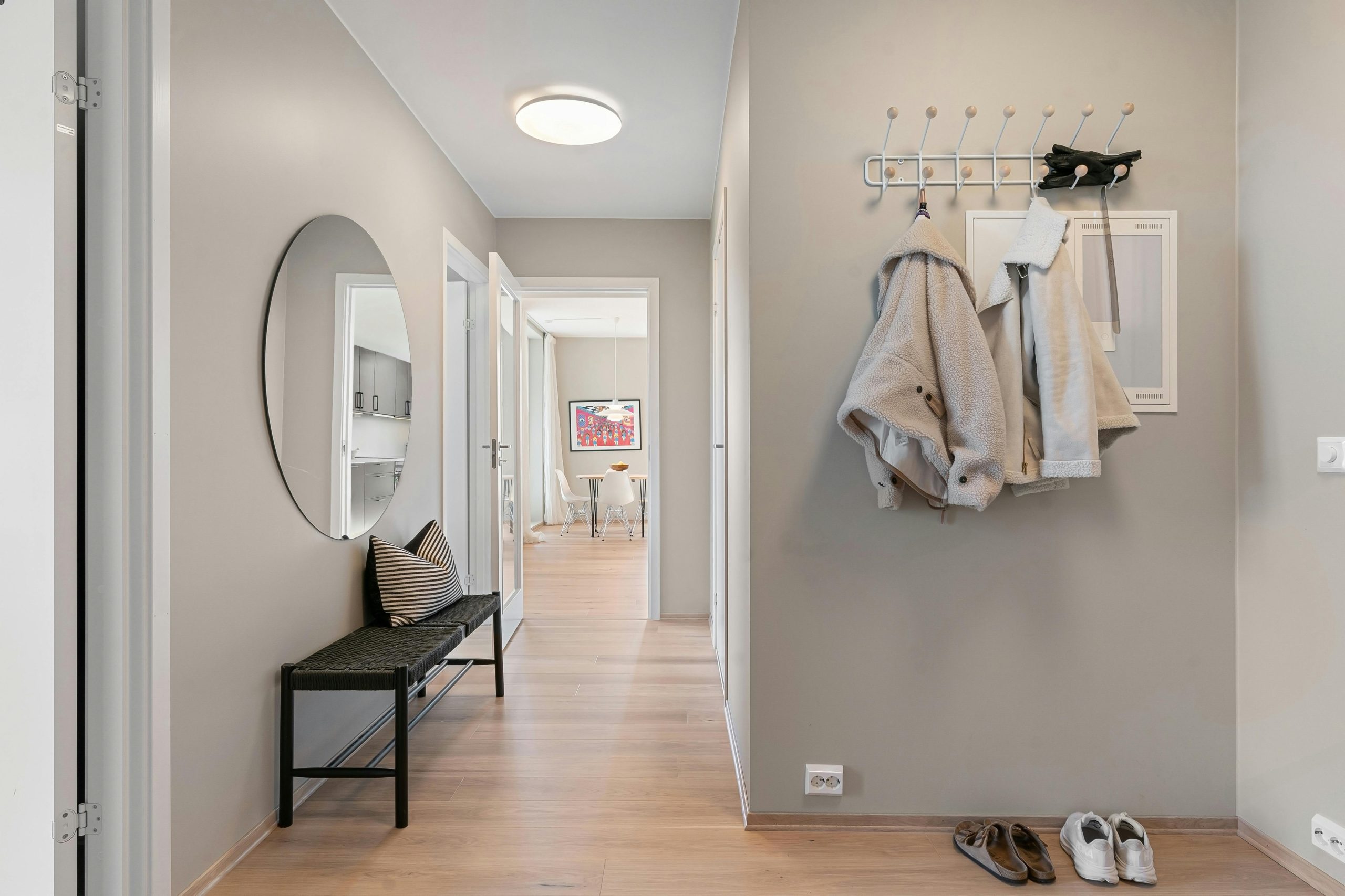 A contemporary hallway with minimalist decor featuring coats, shoes, and a stylish mirror.