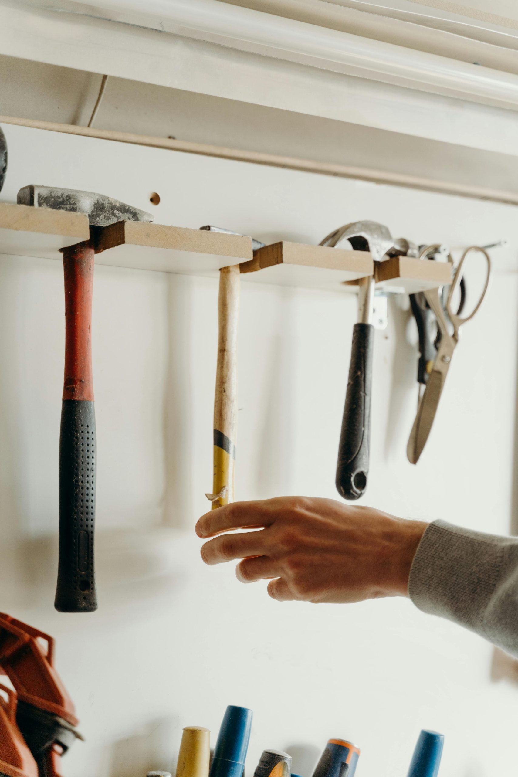 A hand reaches for a tool from a well-organized workshop wall, featuring various hand tools.