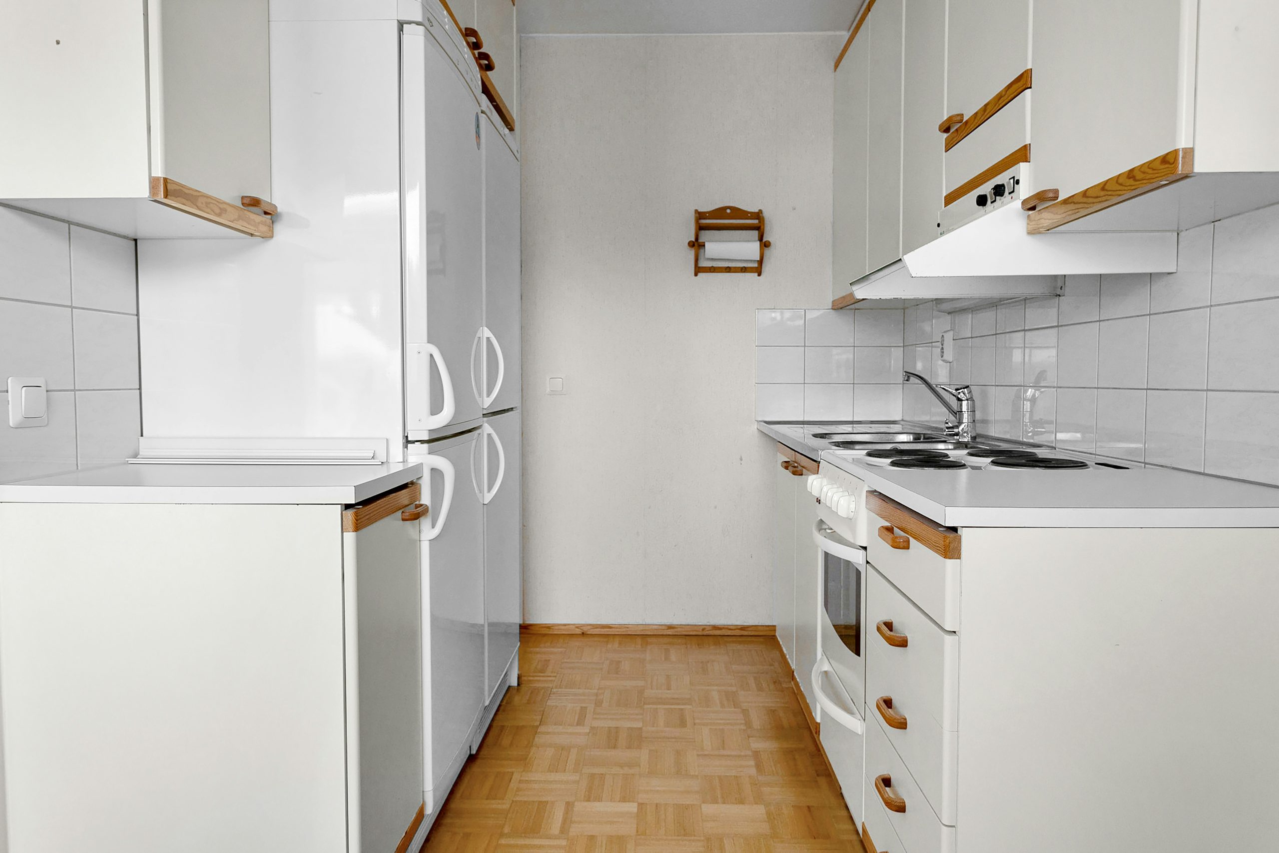 A narrow kitchen with white cabinets and wood floors