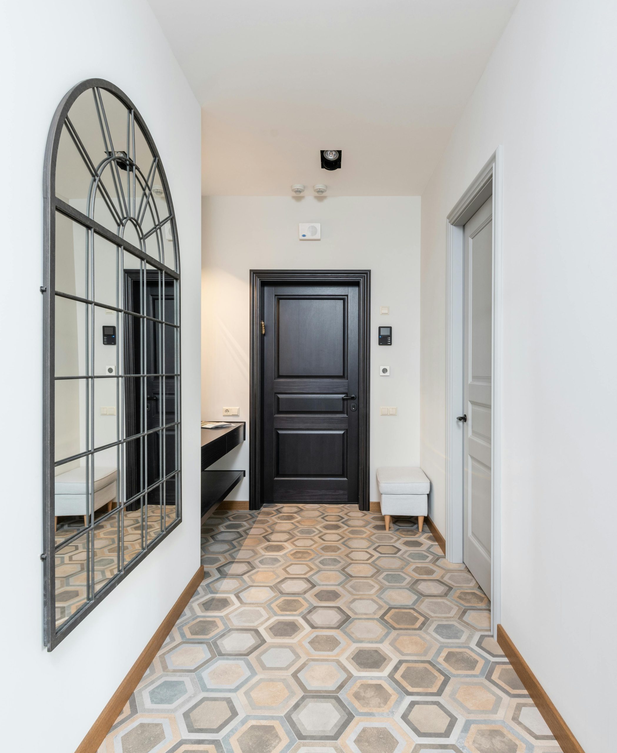 Interior of spacious corridor with colorful tile floor and decorative mirror hanging on light wall placed in contemporary apartment