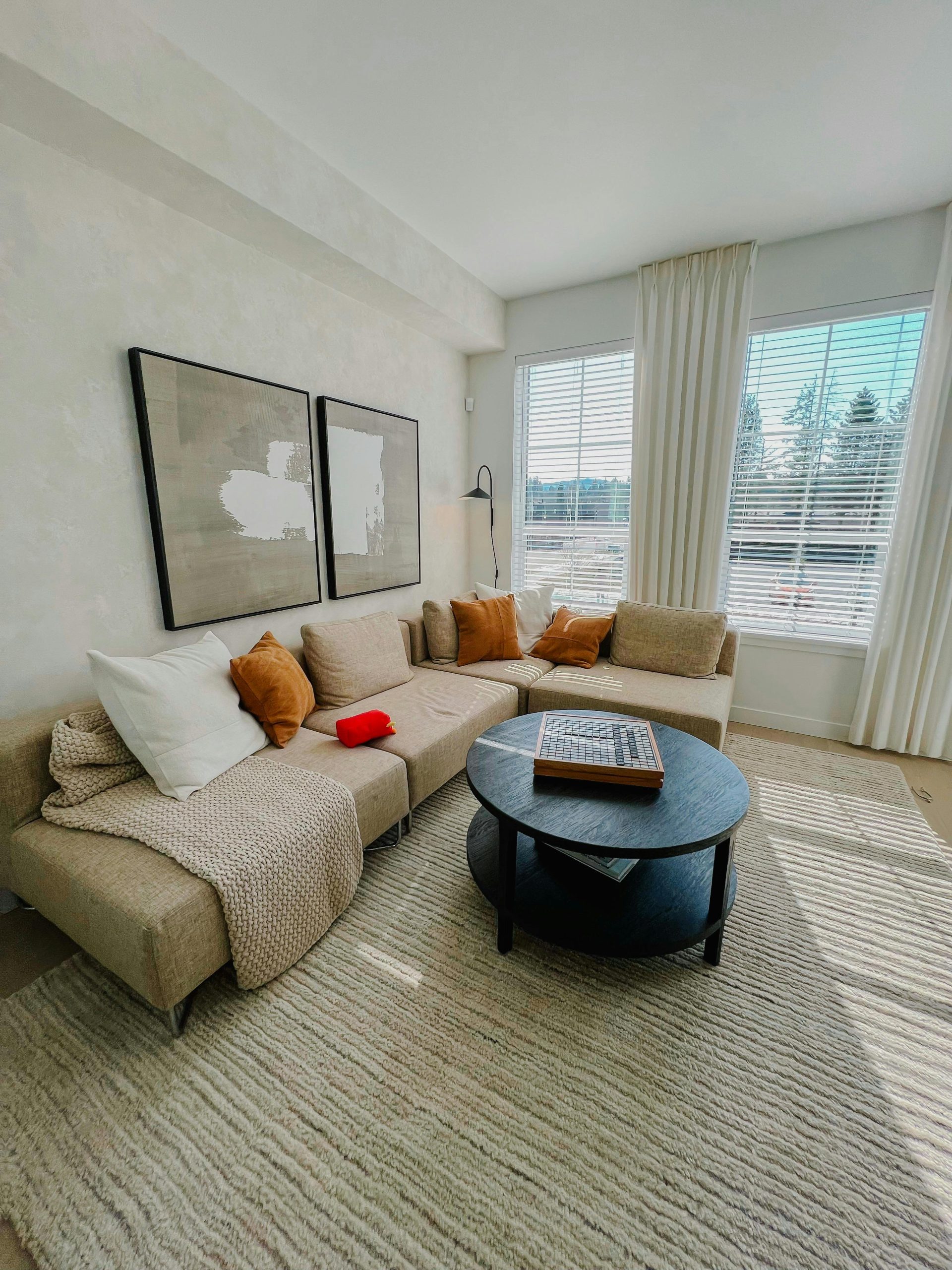 A bright, cozy living room featuring a beige sectional sofa, large windows, and modern decor.
