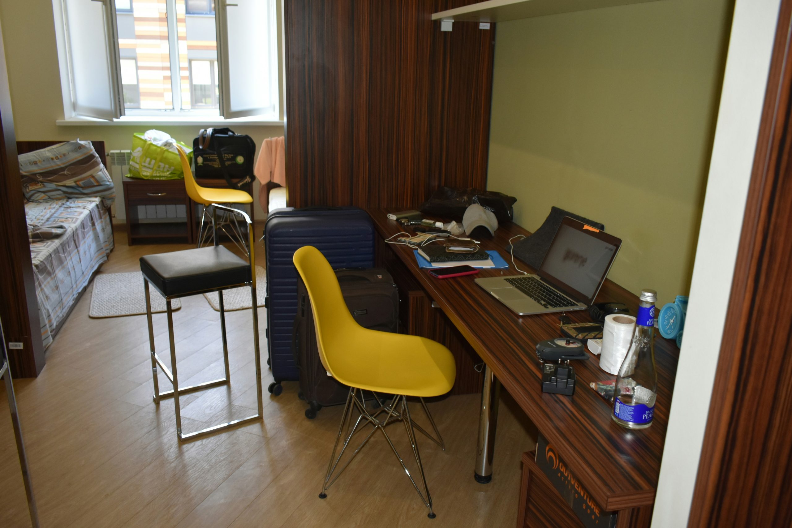 A cluttered room with a desk, chairs, and luggage.