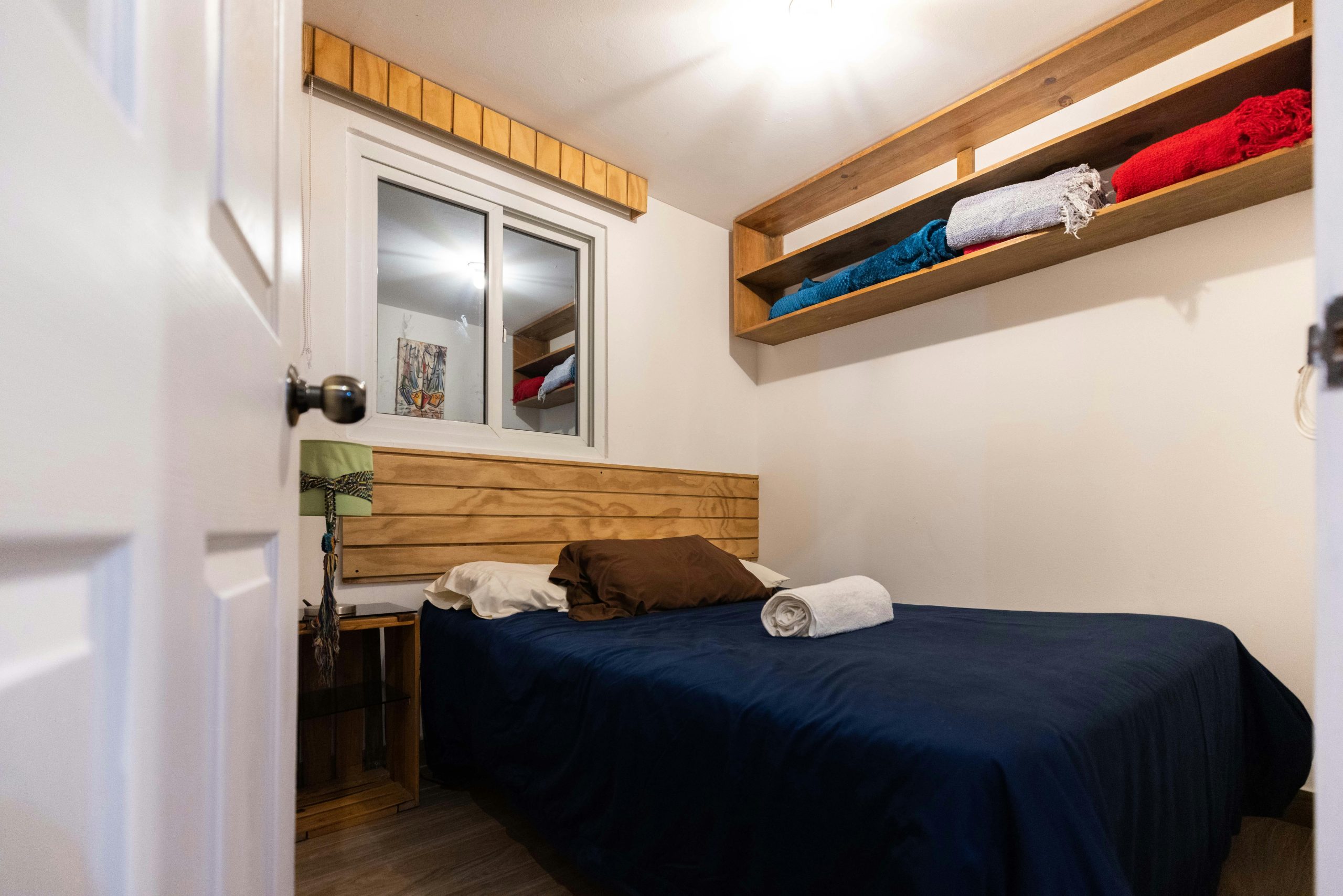 A cozy bedroom featuring a comfy bed, wooden shelves, and natural light.