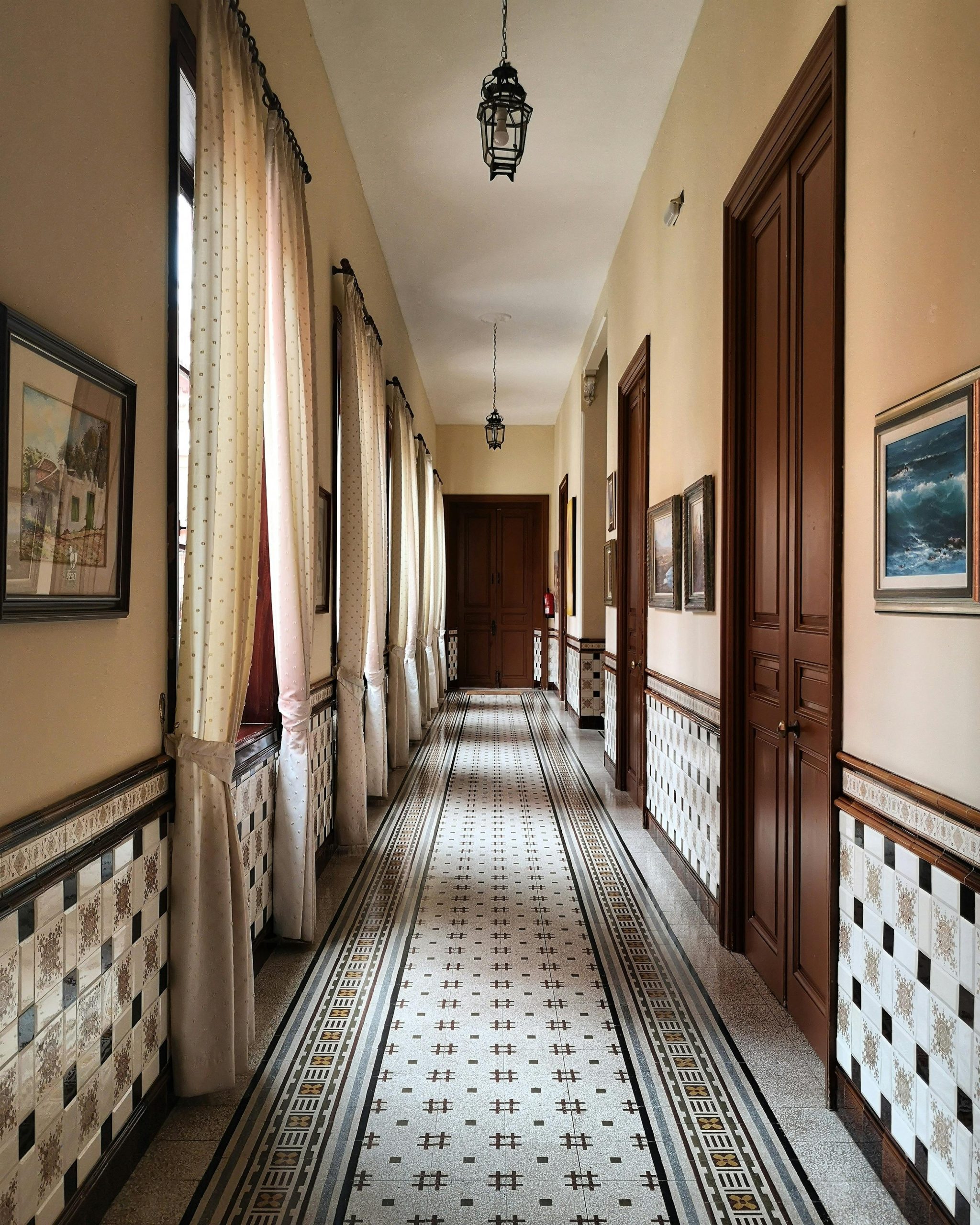 A long, ornate hallway with vintage details, tiles, and artwork in a historical building.