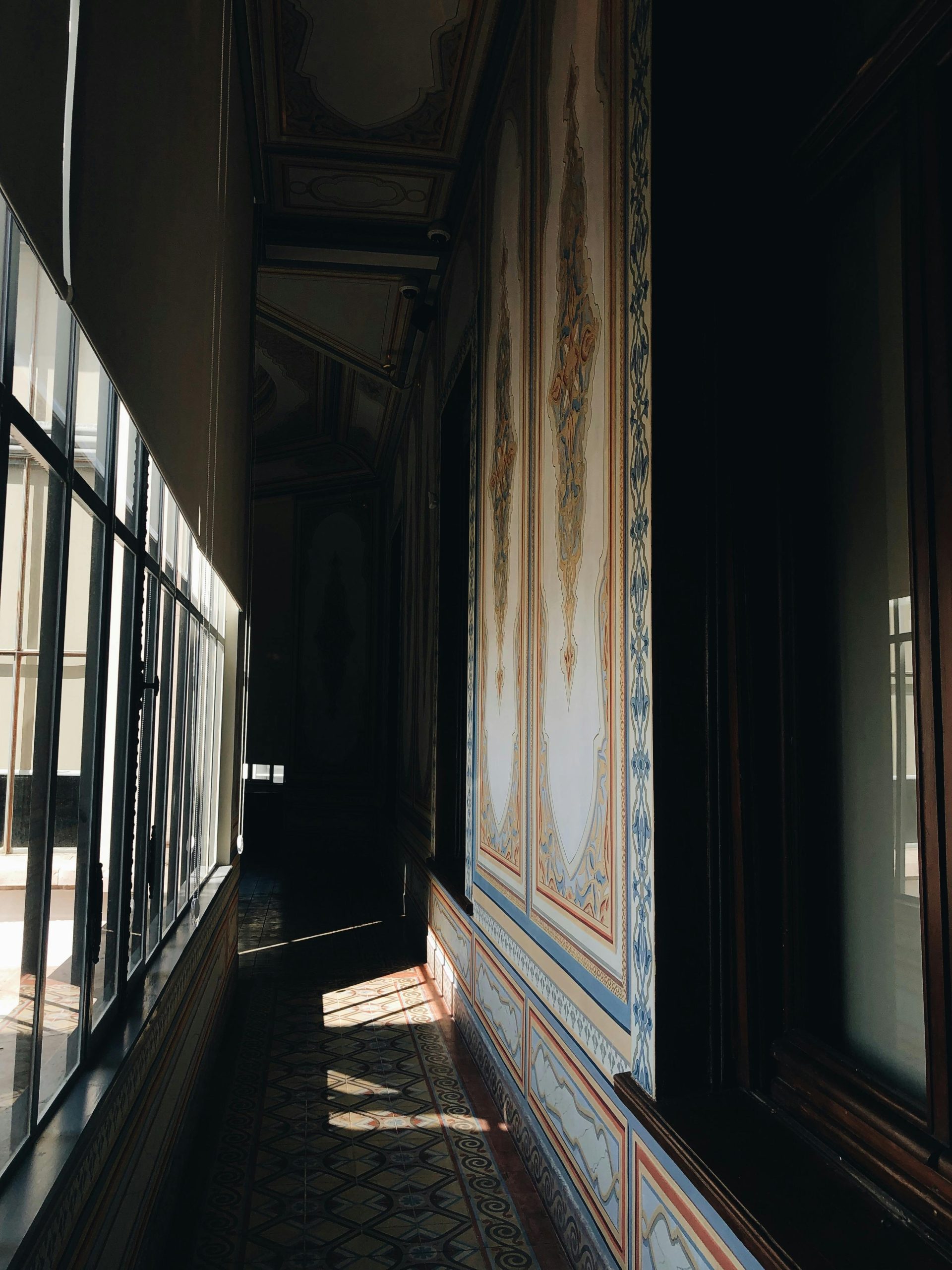 A narrow sunlit corridor with intricate classic wall designs and intricate floor patterns.