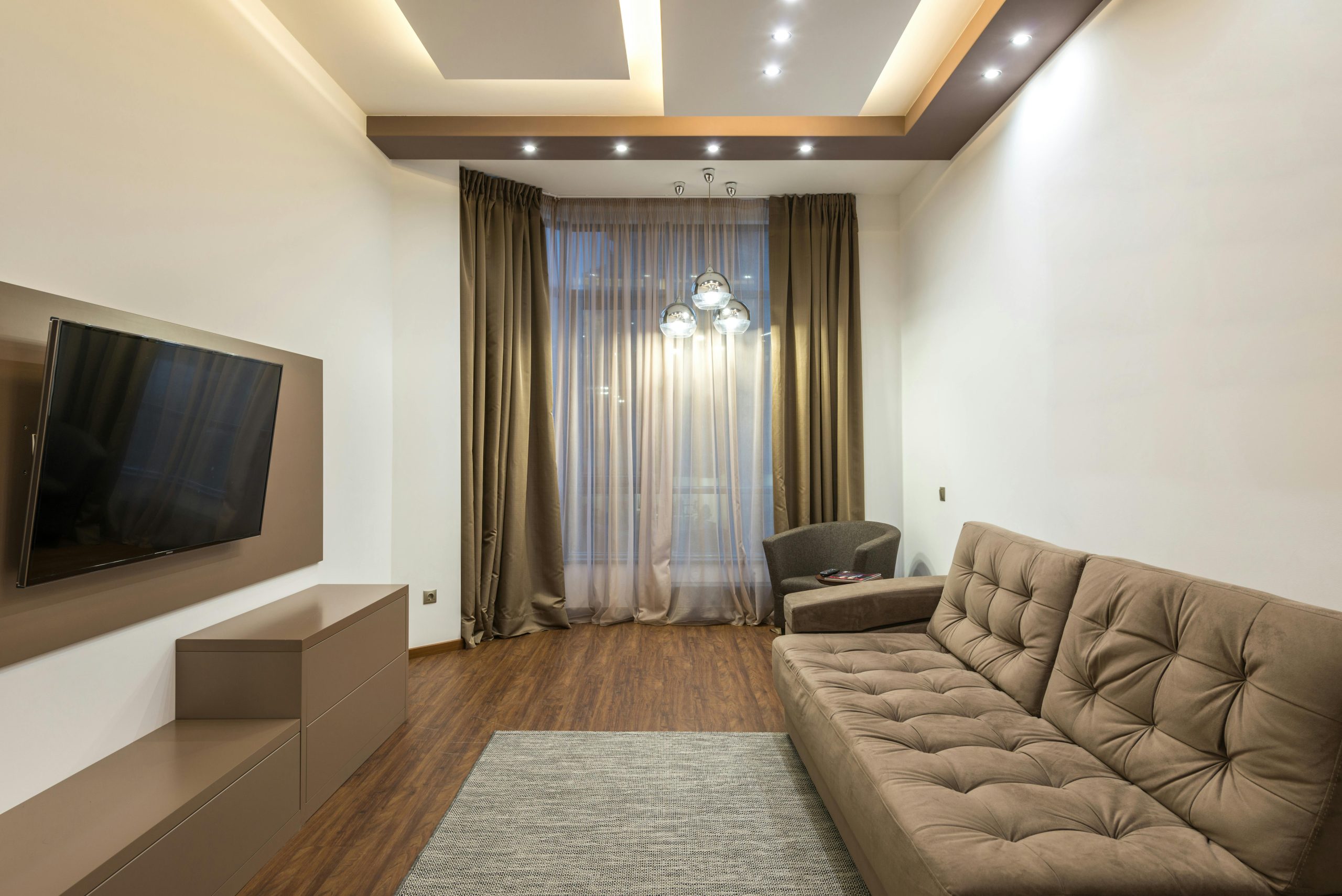 A sleek beige living room featuring a flat screen TV, sofa, and elegant lighting.