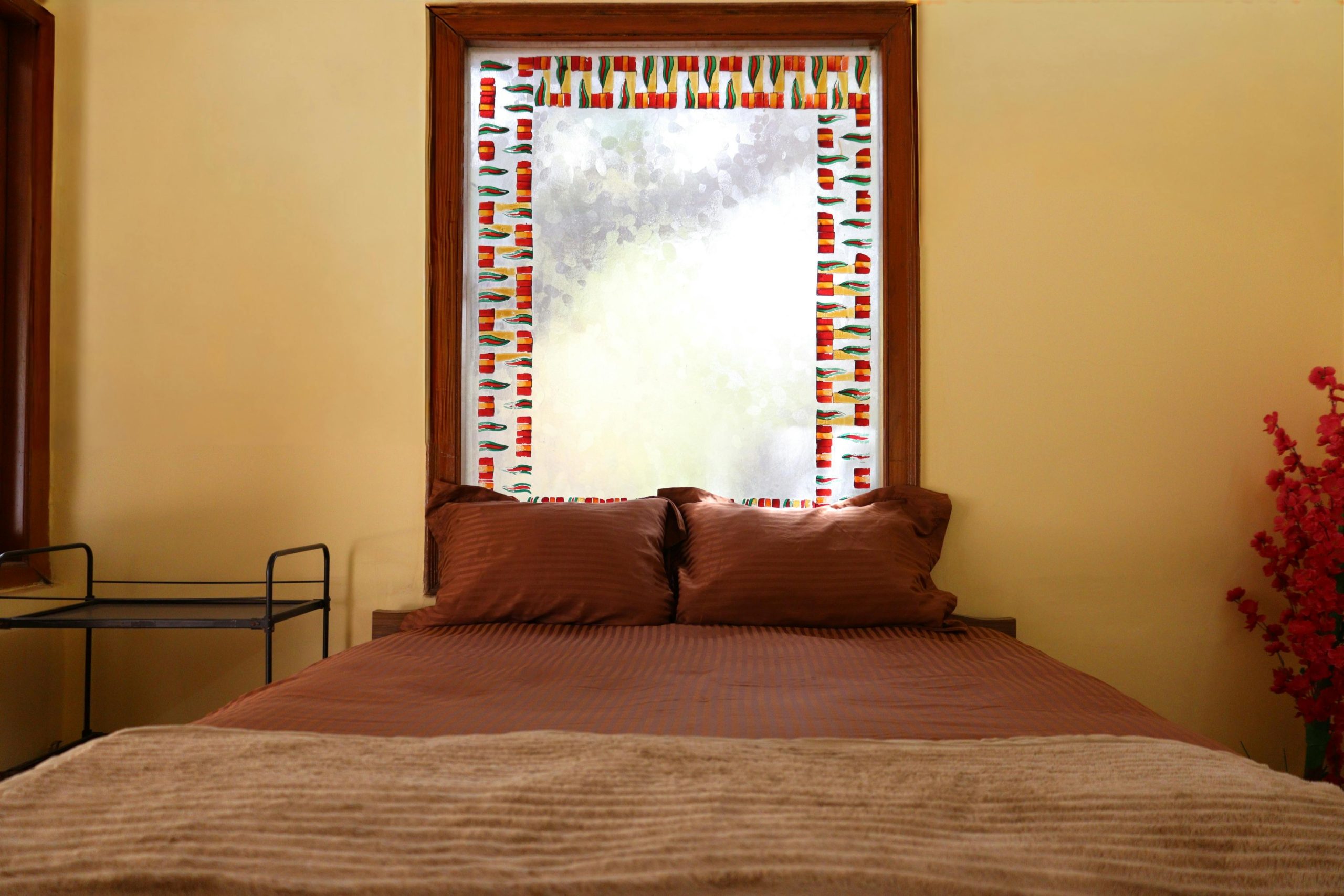 A warm and inviting bedroom with a decorative window and brown bedding in Ahmedabad, India.