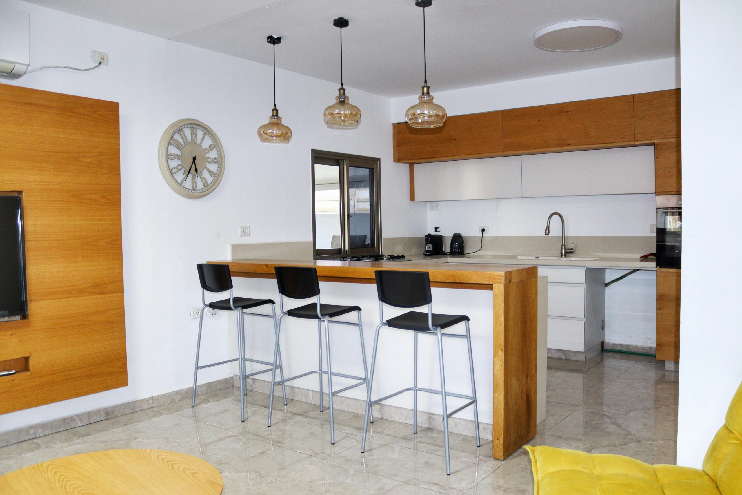 Bright and spacious modern kitchen interior with wooden cabinets and counter, bar stools, and pendant lighting.