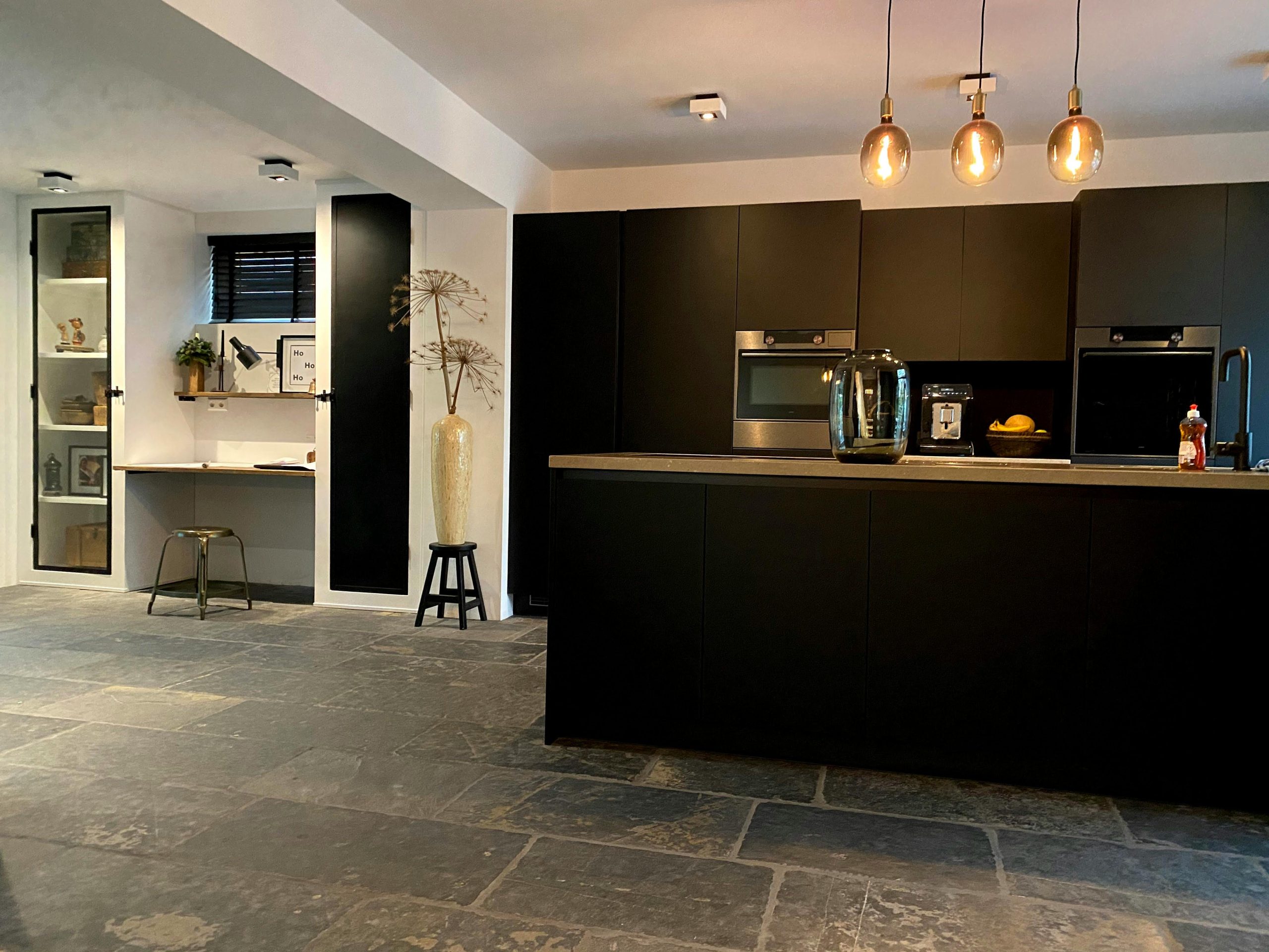 Contemporary kitchen featuring black cabinets, stone flooring, and minimalist decor accentuated by pendant lighting.
