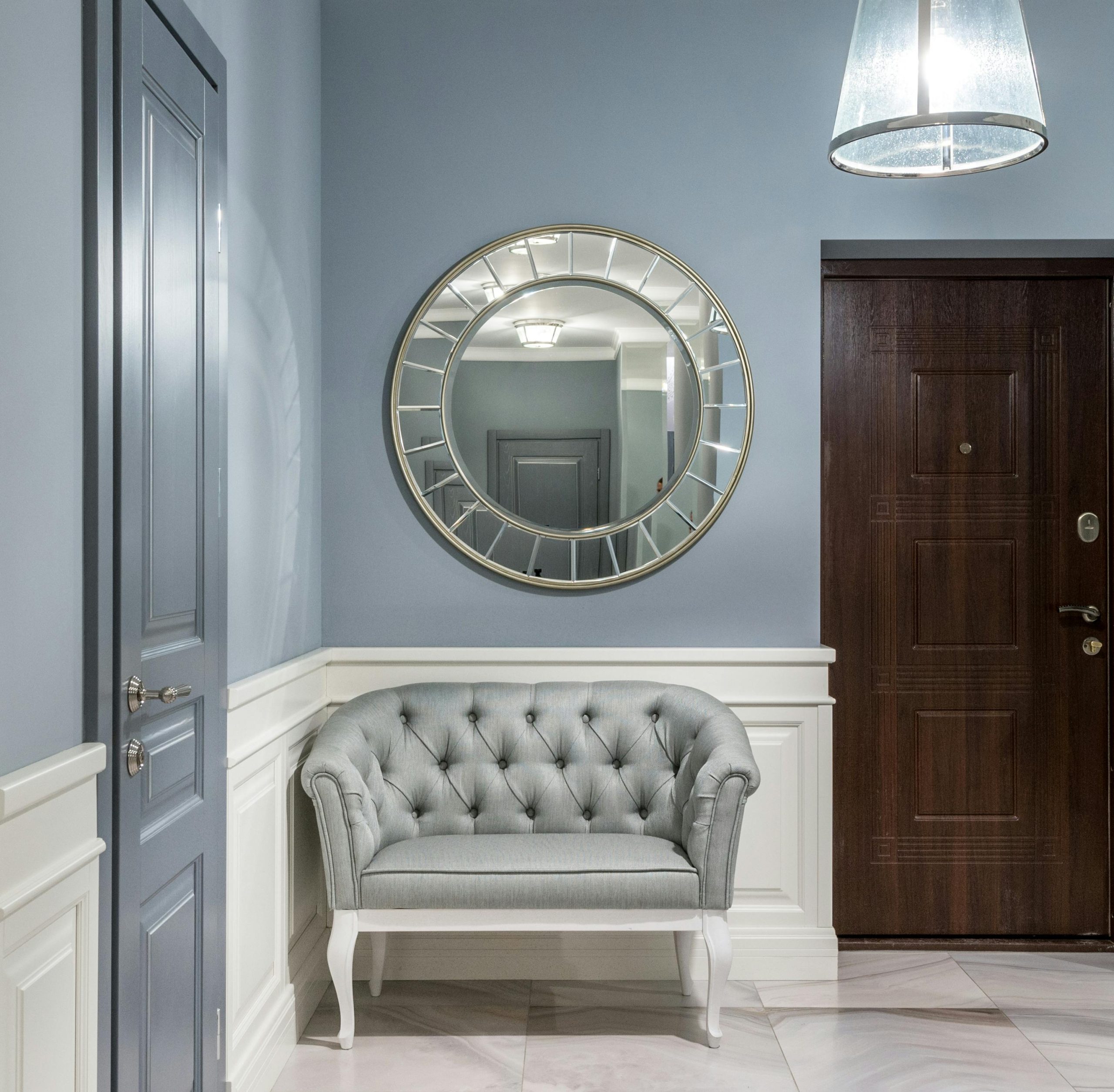 Gray leather armchair placed under stylish round mirror in light corridor with gray walls in contemporary apartment in daytime