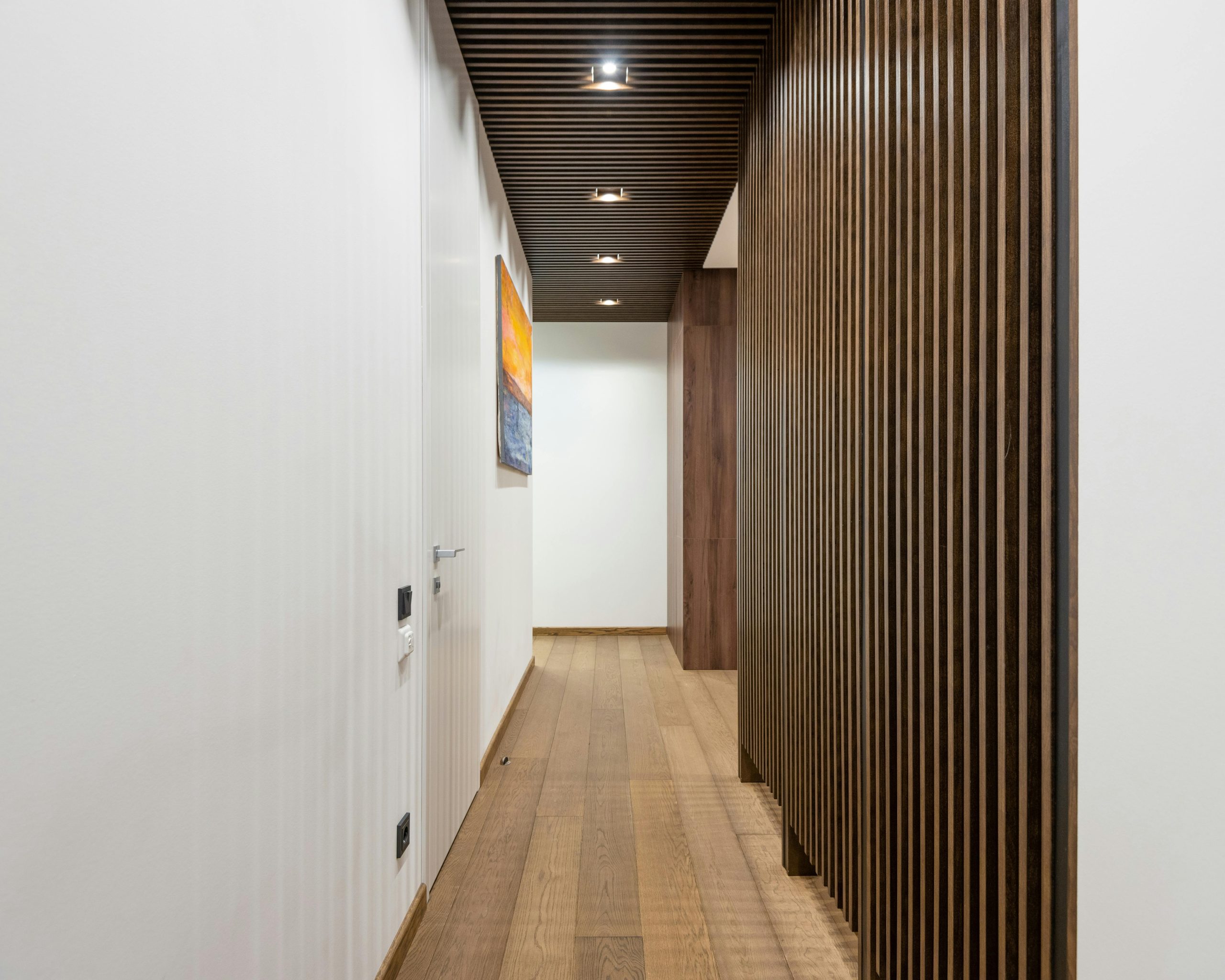 Interior of modern hallway with decorative wooden elements and white wall with door and painting in modern apartment with creative design