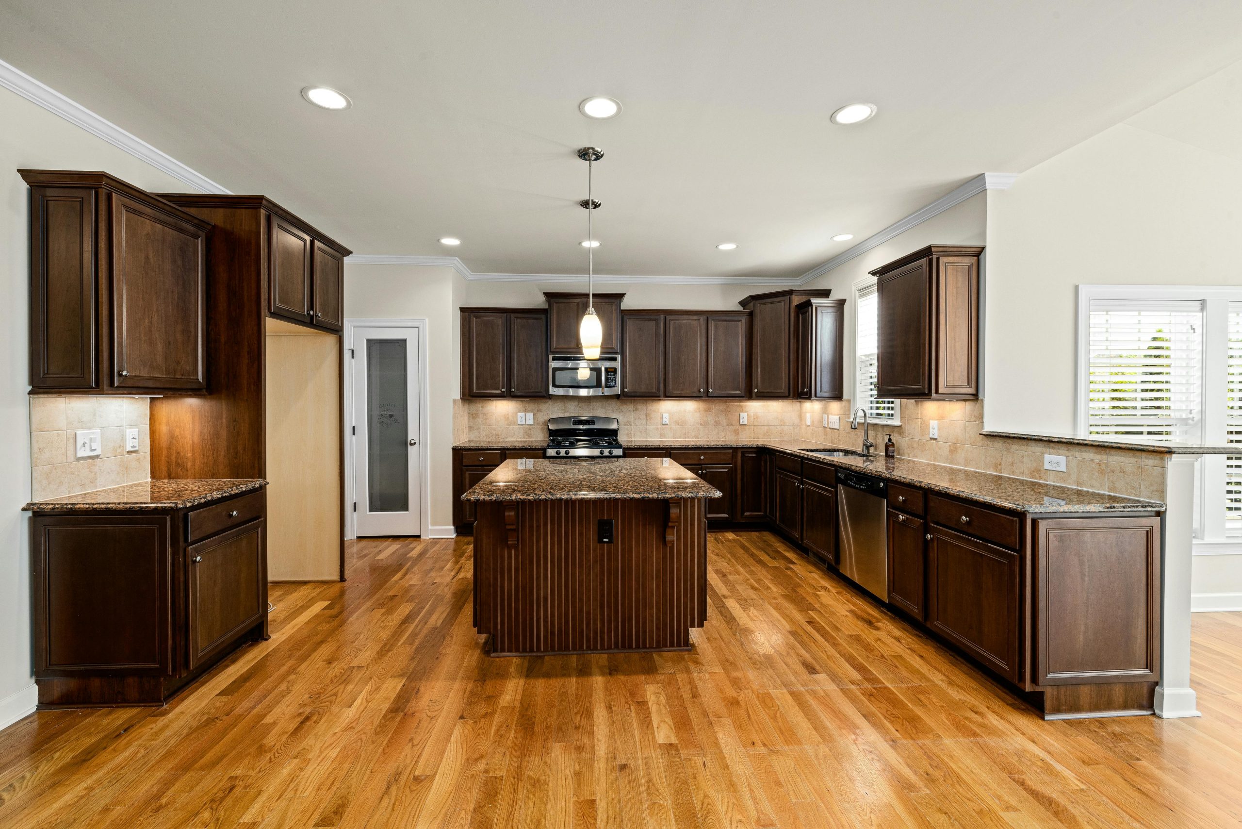 Luxurious wooden kitchen featuring dark cabinets, island, and stainless steel appliances.