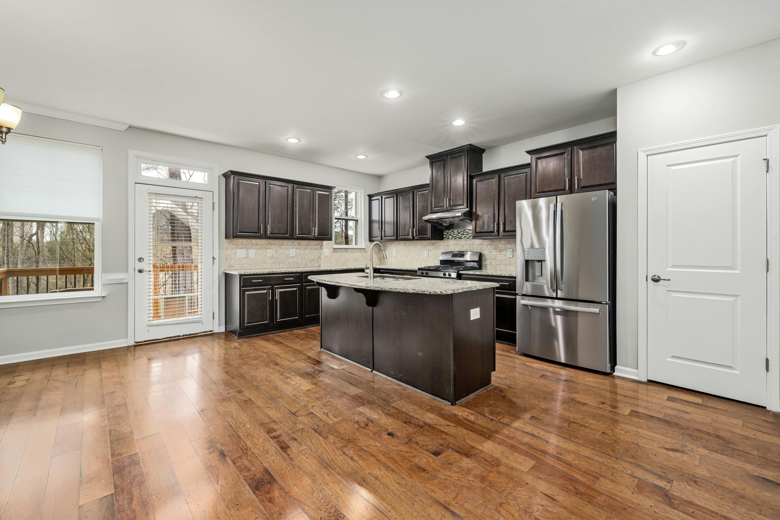 Spacious modern kitchen featuring dark wood cabinets, island, and stainless steel appliances.