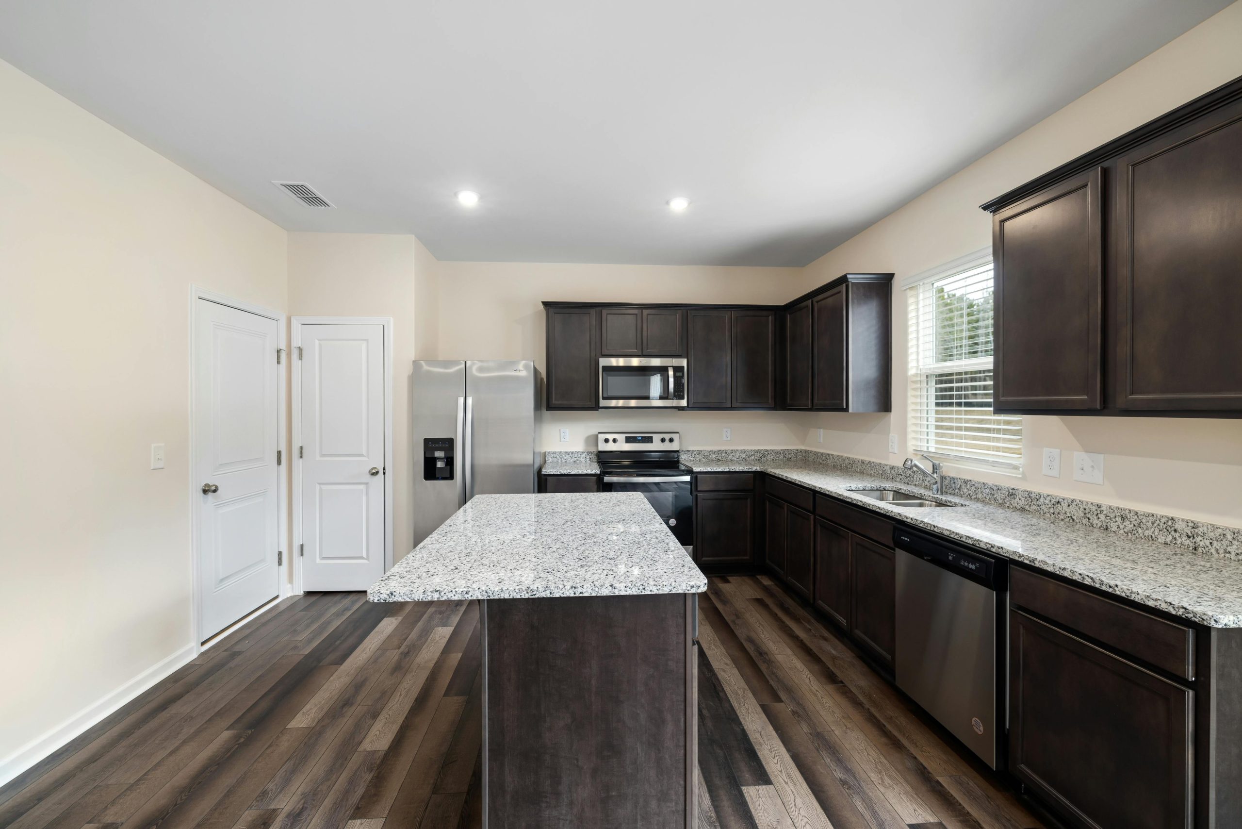 Spacious modern kitchen featuring granite countertops and dark wood cabinetry with stainless steel appliances.