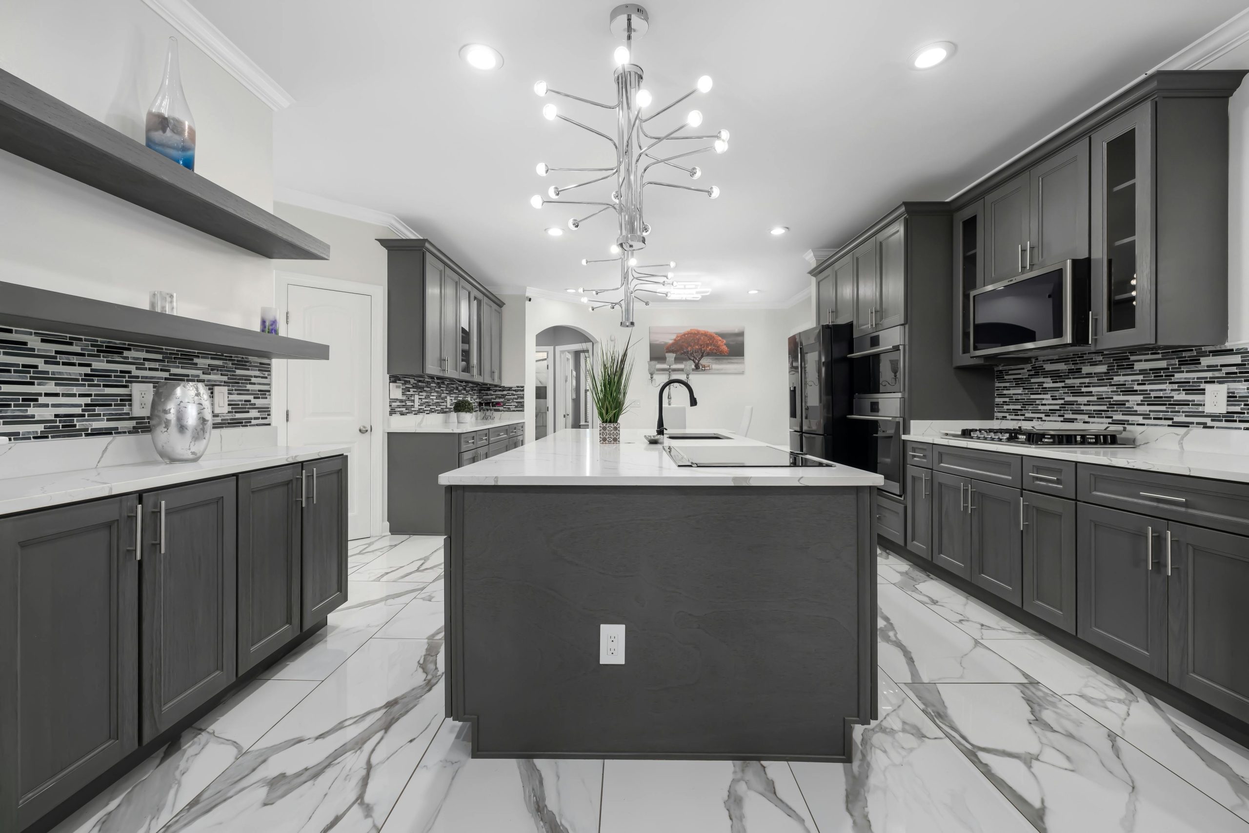 Spacious modern kitchen with grey cabinets and marble floors, featuring contemporary lighting.