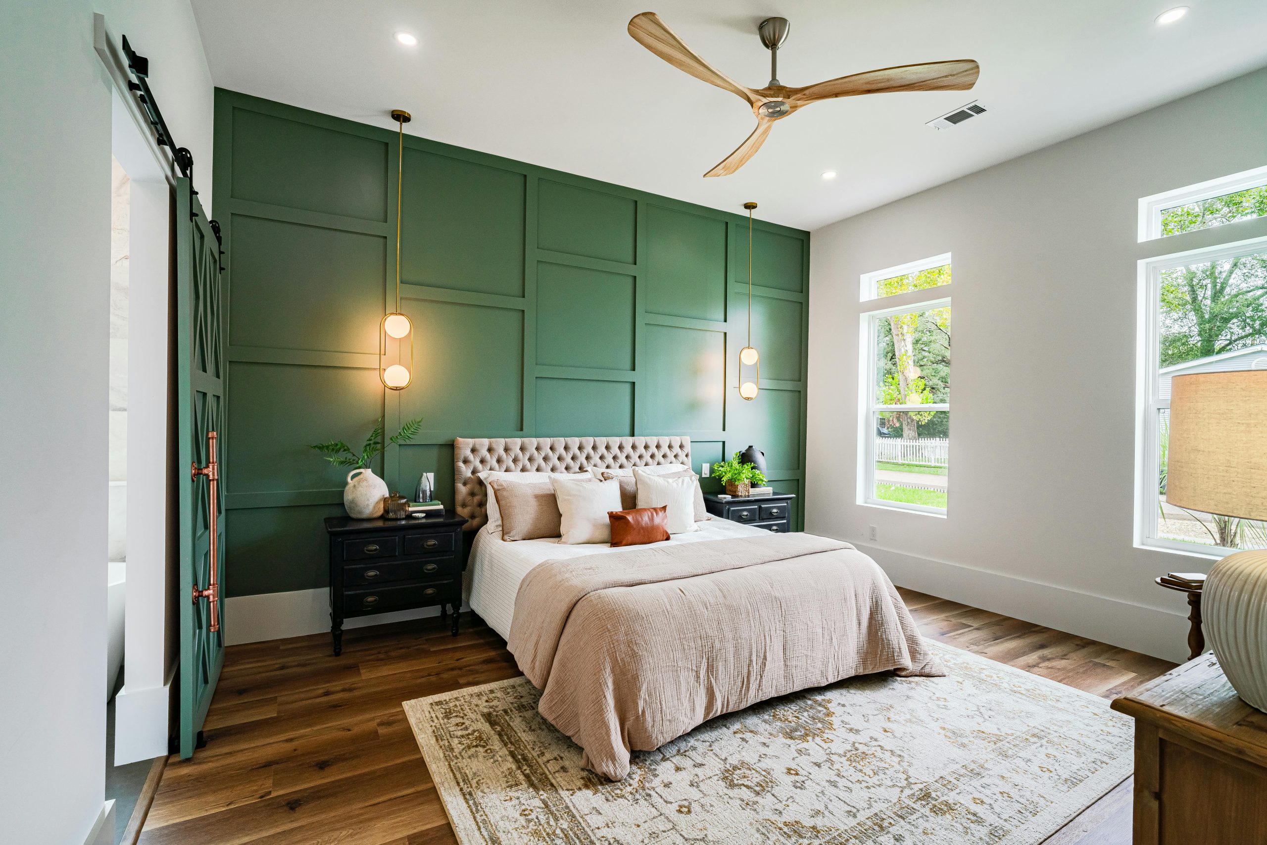 Stylish bedroom with green panel accent wall, neutral decor, and natural light streaming through large windows.