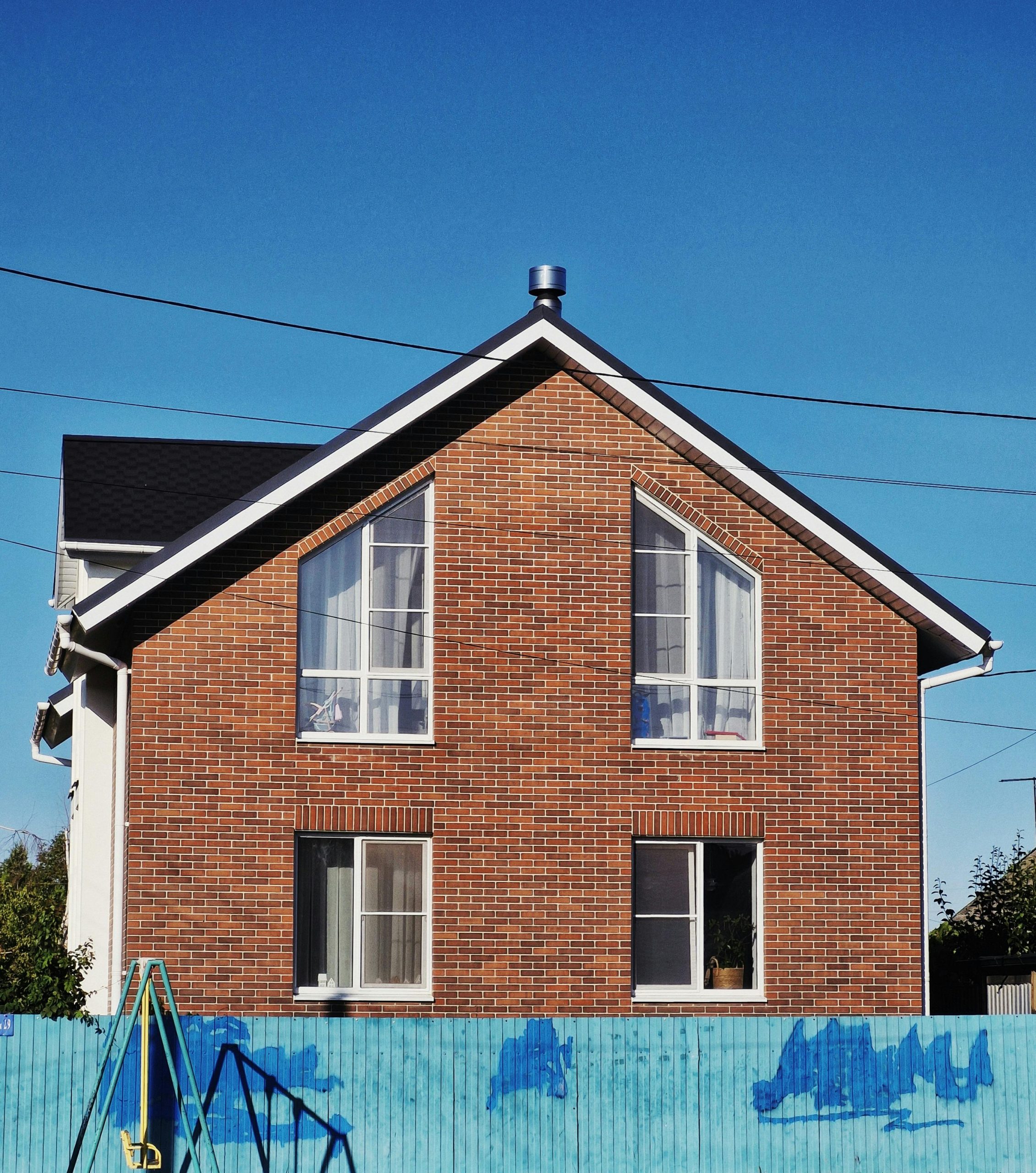 A charming brick house with large windows, set against a clear blue sky, perfect for real estate and architecture themes.