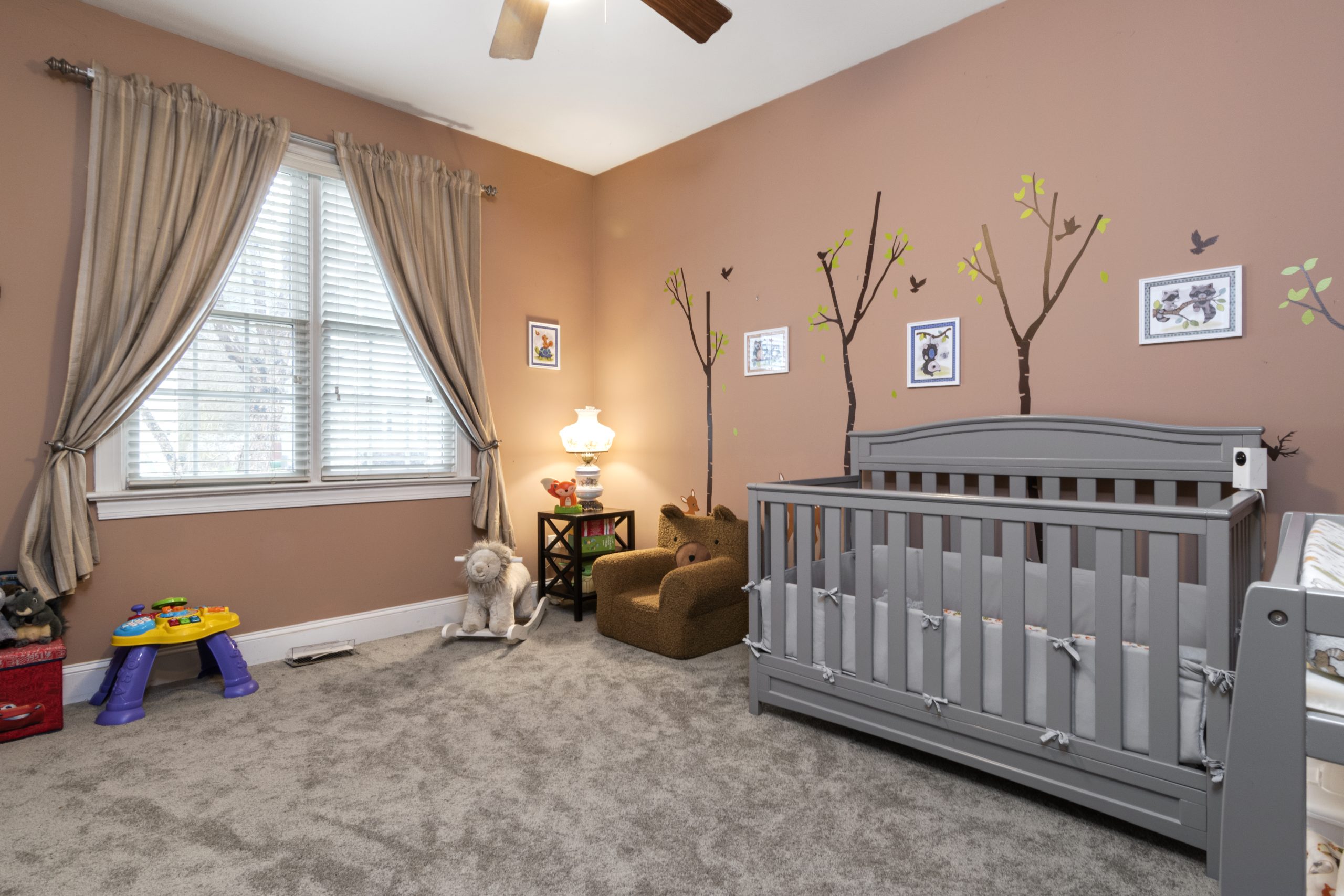 A cozy nursery featuring a grey crib, toys, and tree wall art with soft lighting.