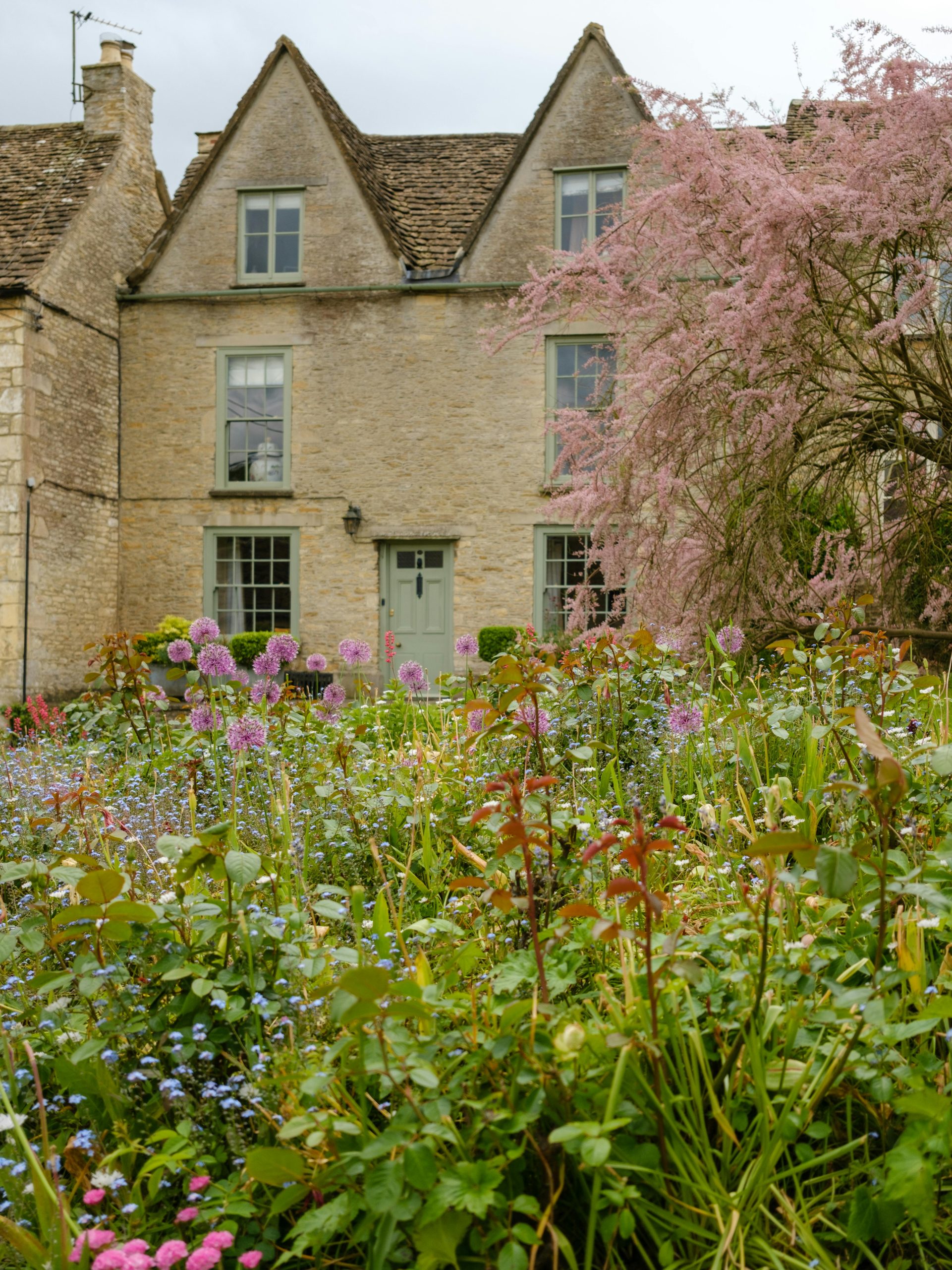 A picturesque stone cottage surrounded by vibrant spring blooms under a soft daylight sky.