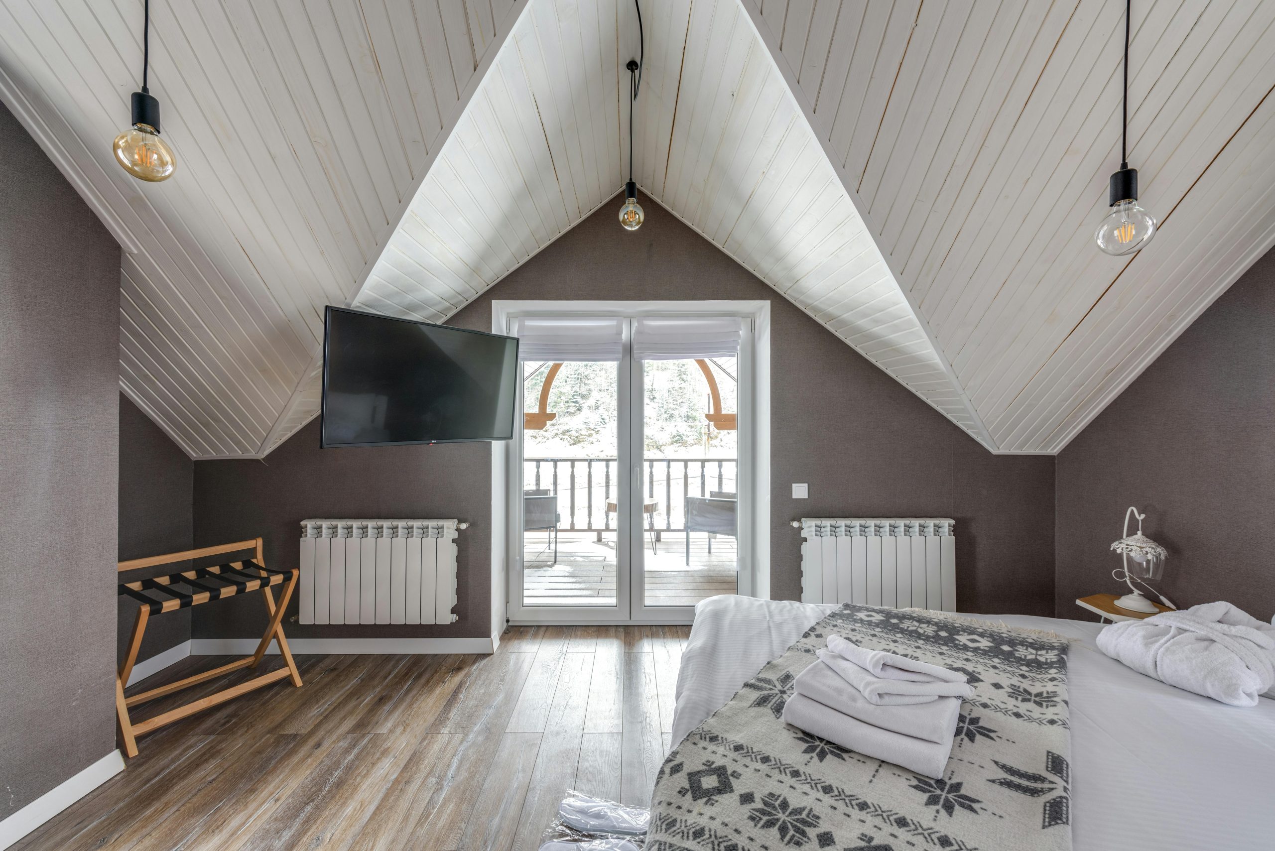 A serene attic bedroom featuring a balcony, TV, and decorative lights.