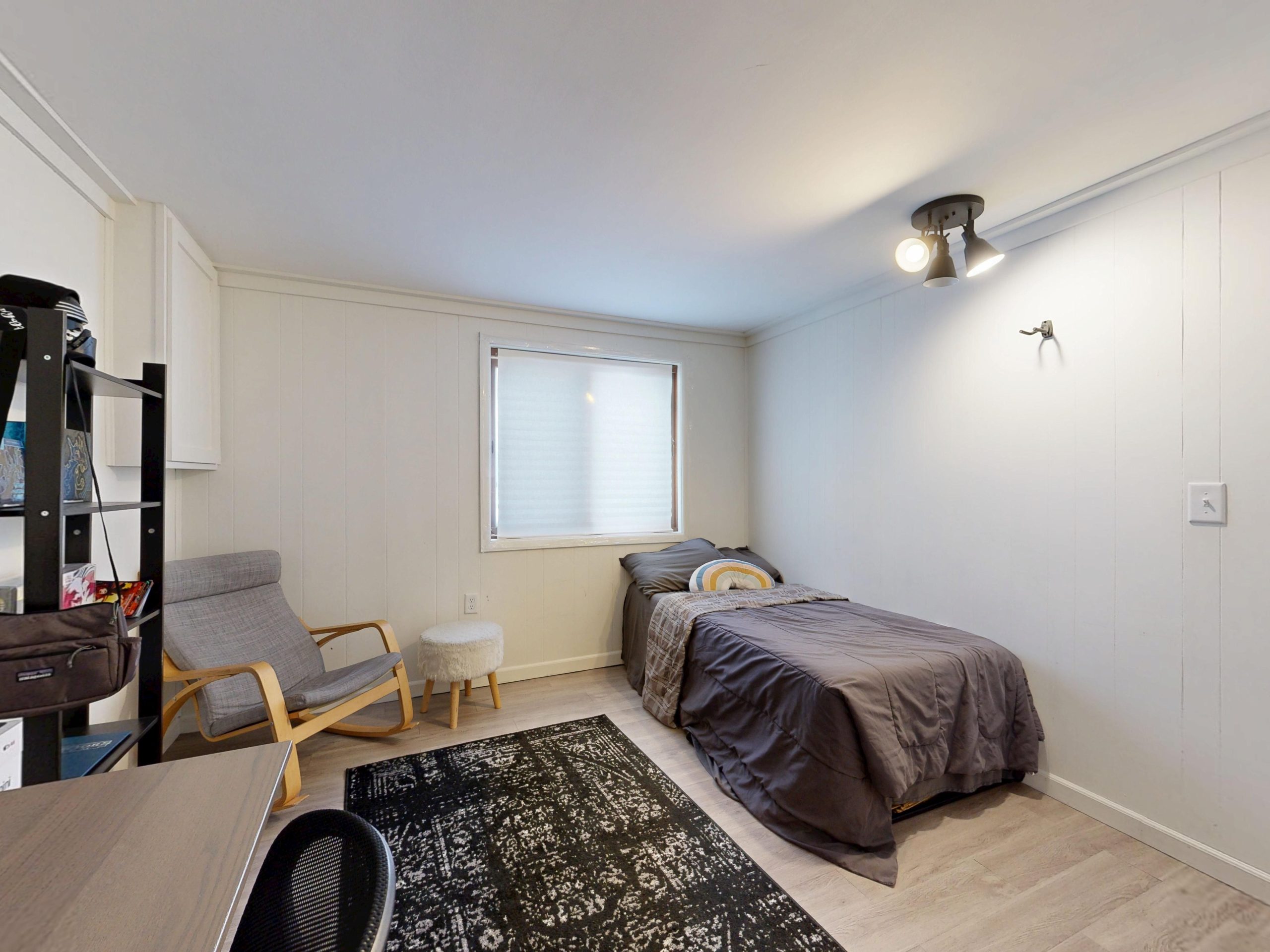 A simple minimalist bedroom with a grey bedspread, armchair, and modern decor.