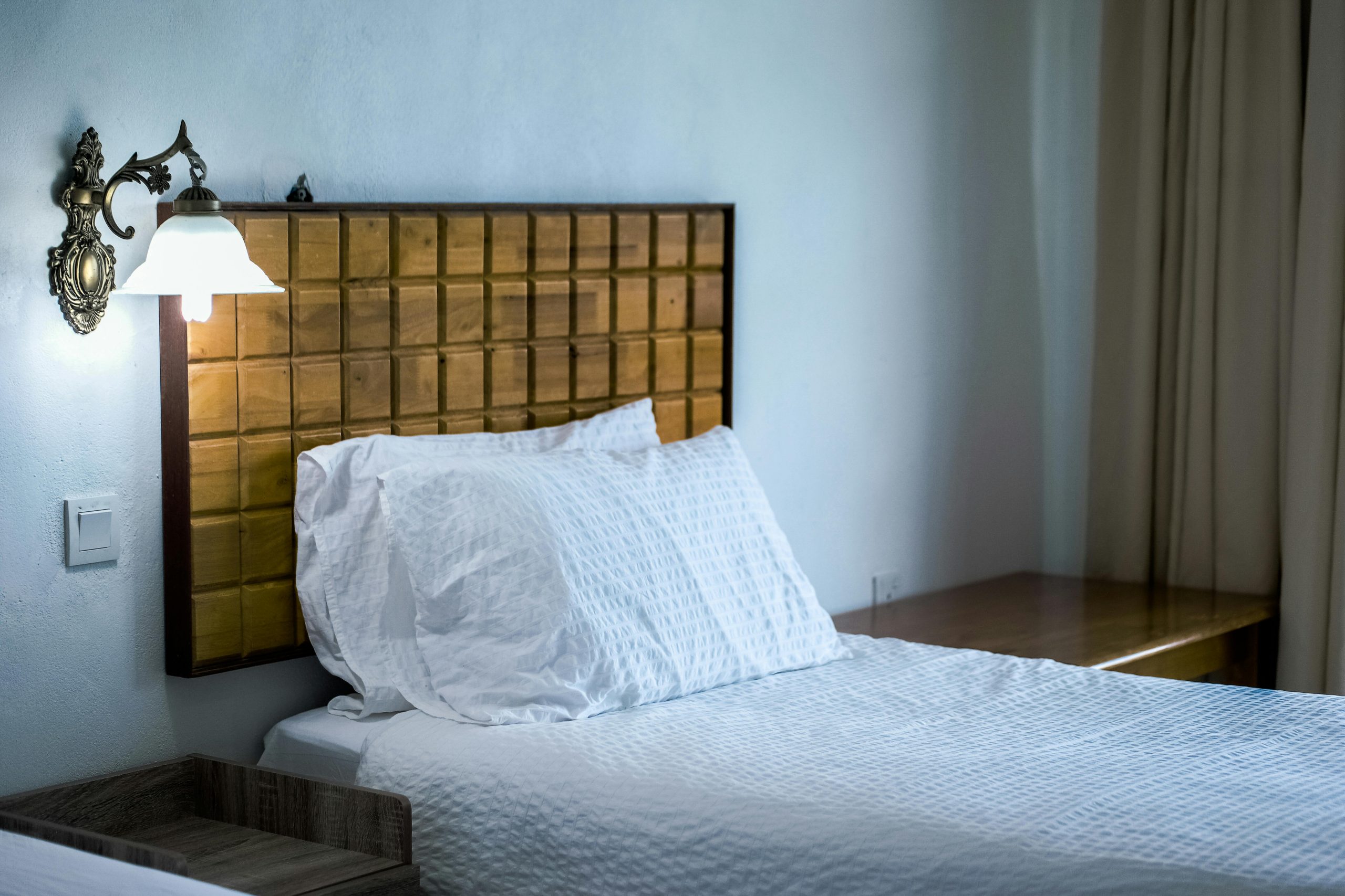 A stylish bedroom featuring a wooden headboard, wall lamp, and white bedding.