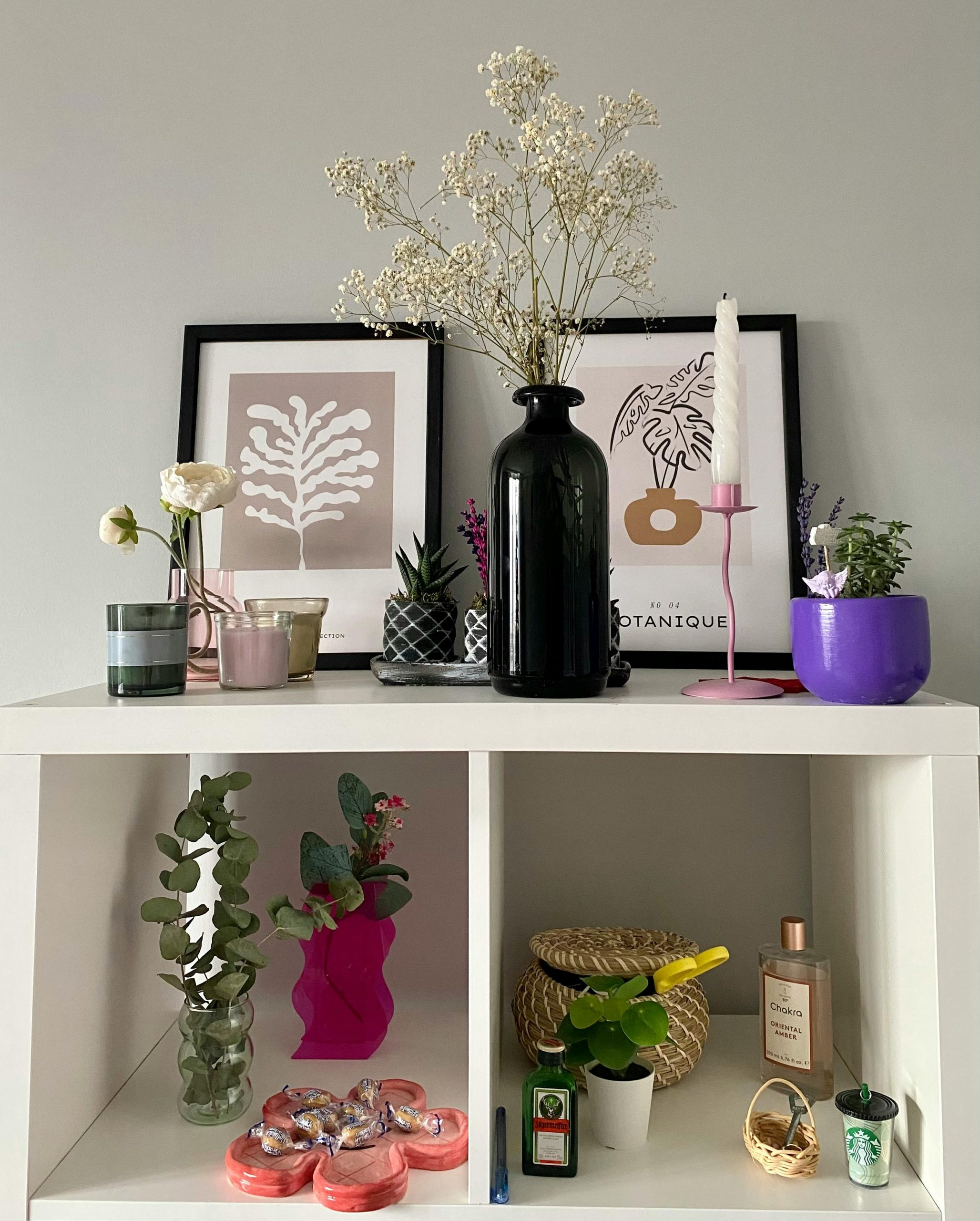A stylish modern shelf featuring vases, plants, and artistic framed prints for interior decoration.