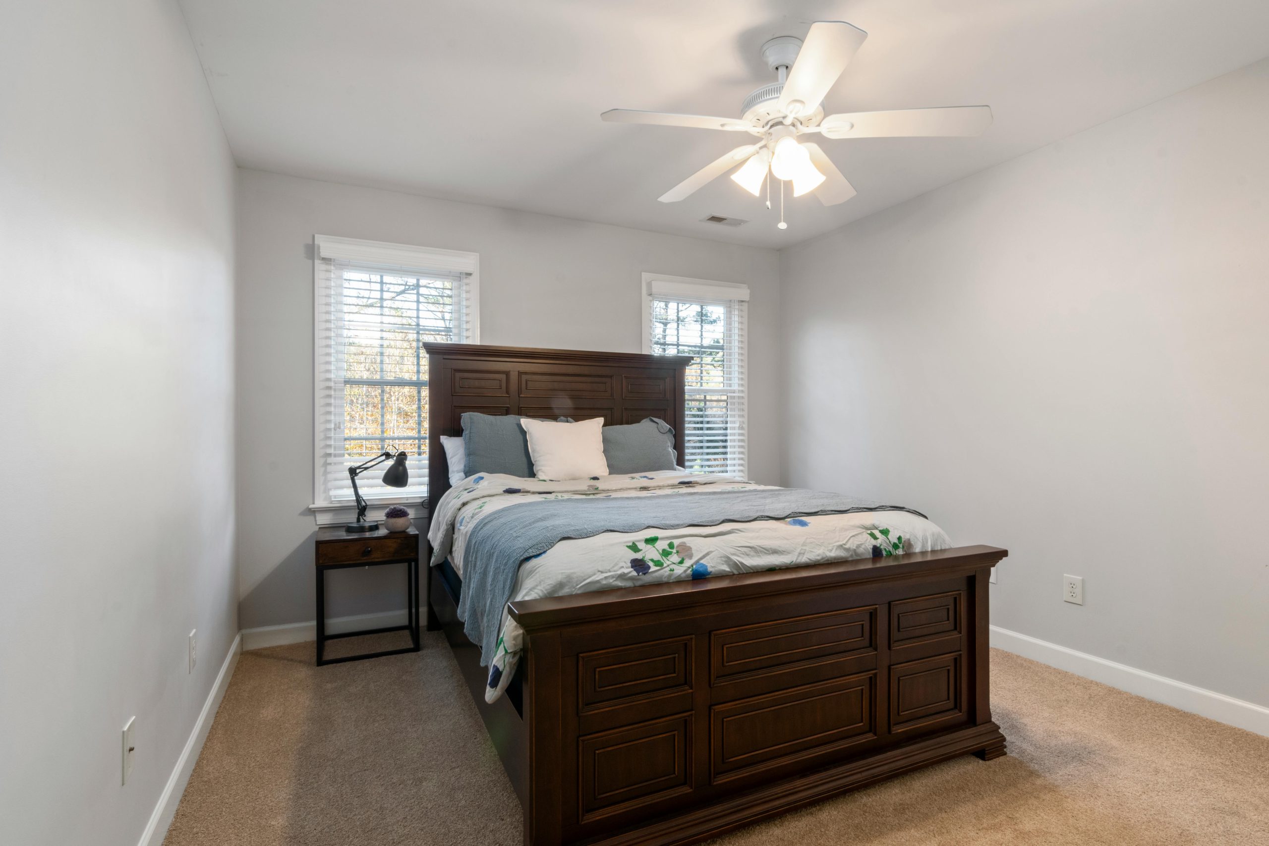 A well-lit bedroom featuring a wooden bed, nightstand, and ceiling fan for a comfortable ambiance.