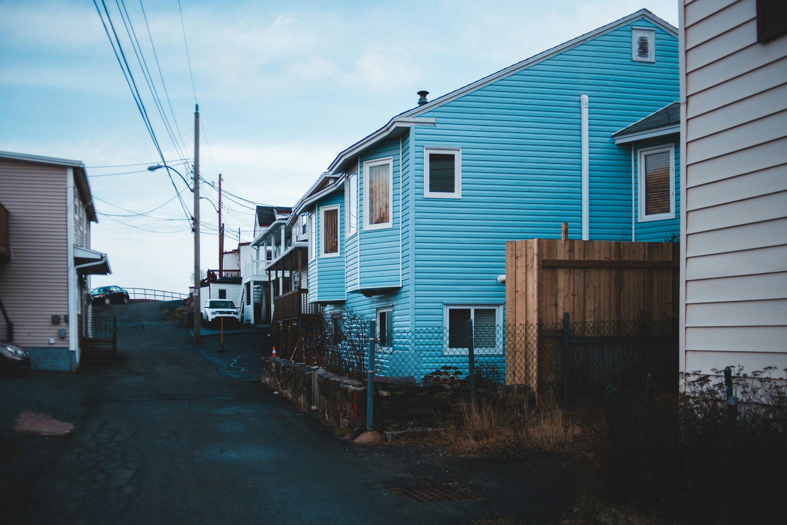 Asphalt roadway with car and wire posts between contemporary dwelling building facades under cloudy sky in daytime