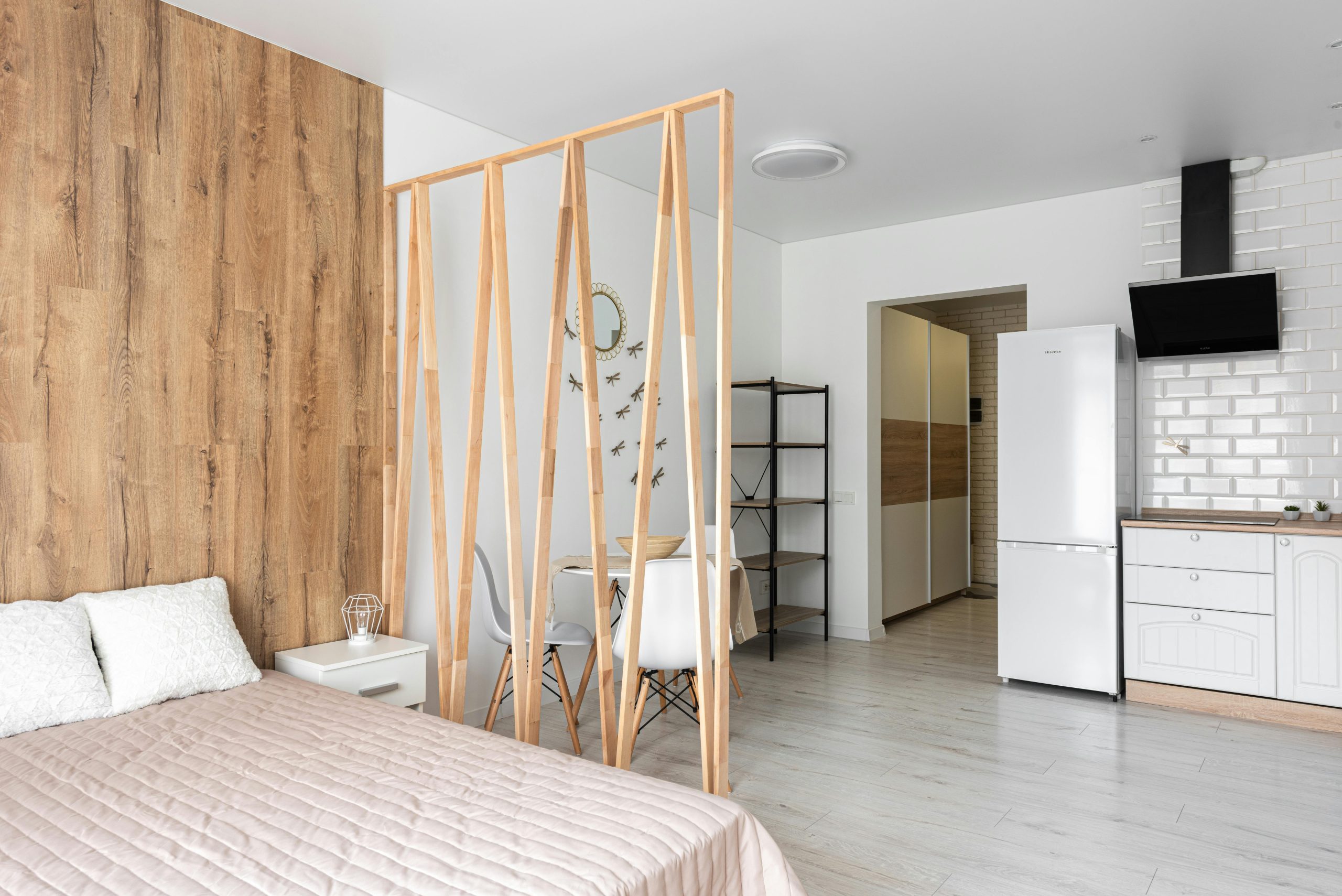Bed with cushions and cover against wooden partition and fridge on parquet with chairs at home in daylight