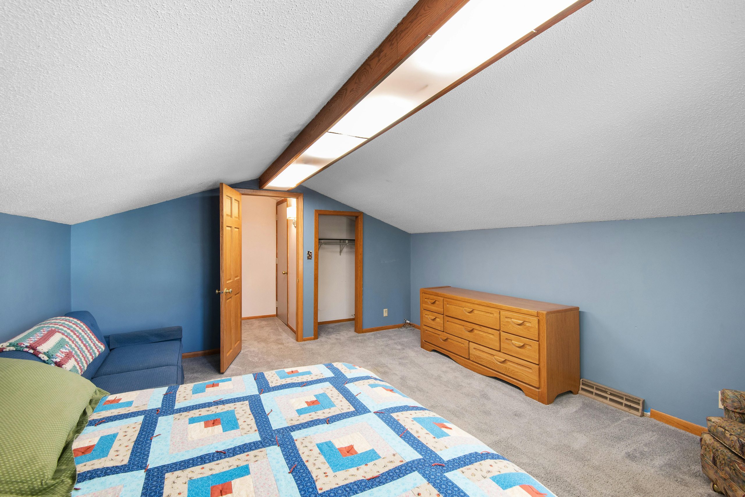 Bright attic bedroom featuring a colorful quilt, wooden dresser, and cozy ambiance.