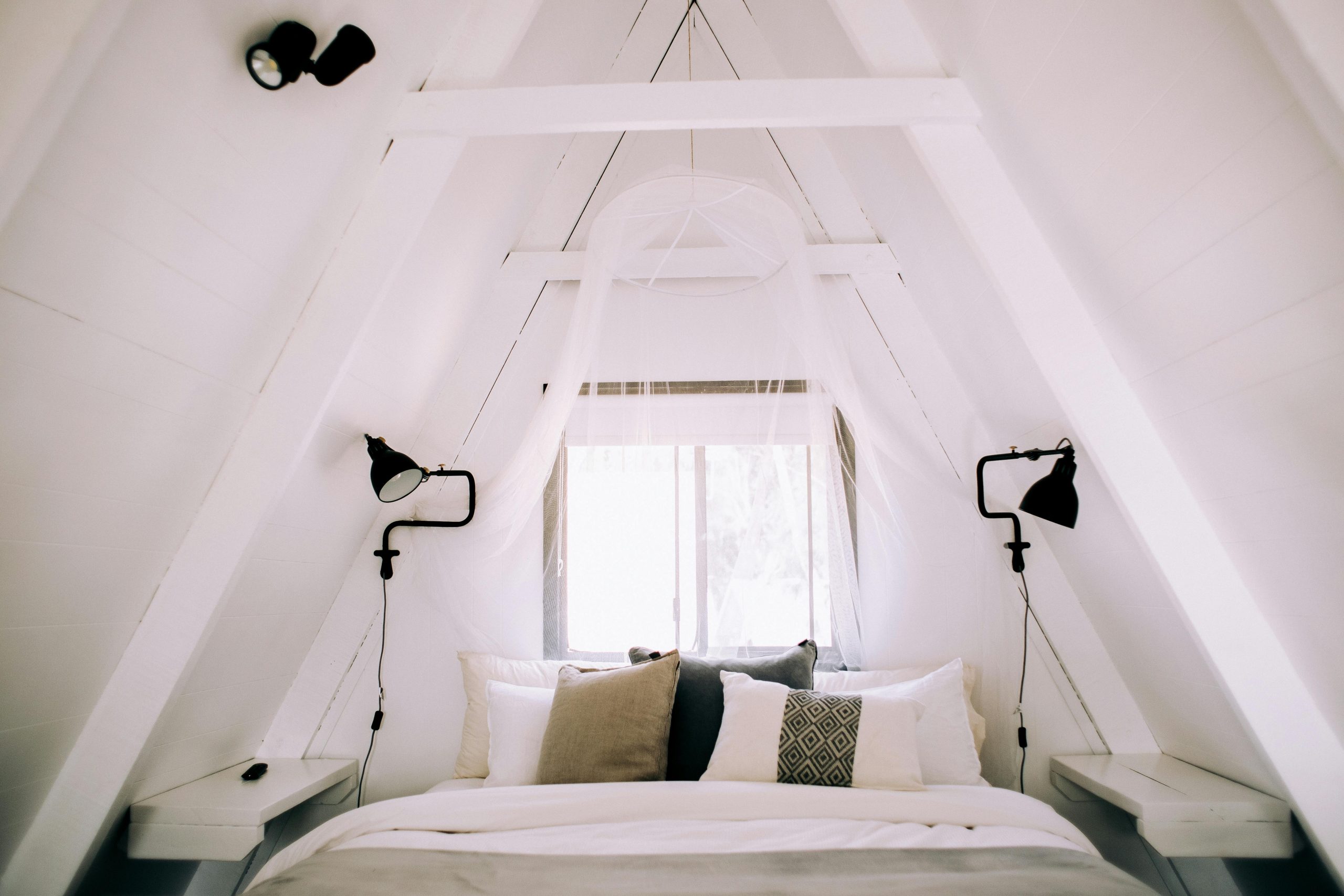 Bright white A-frame bedroom with cozy decor and pillows, perfect for relaxation.