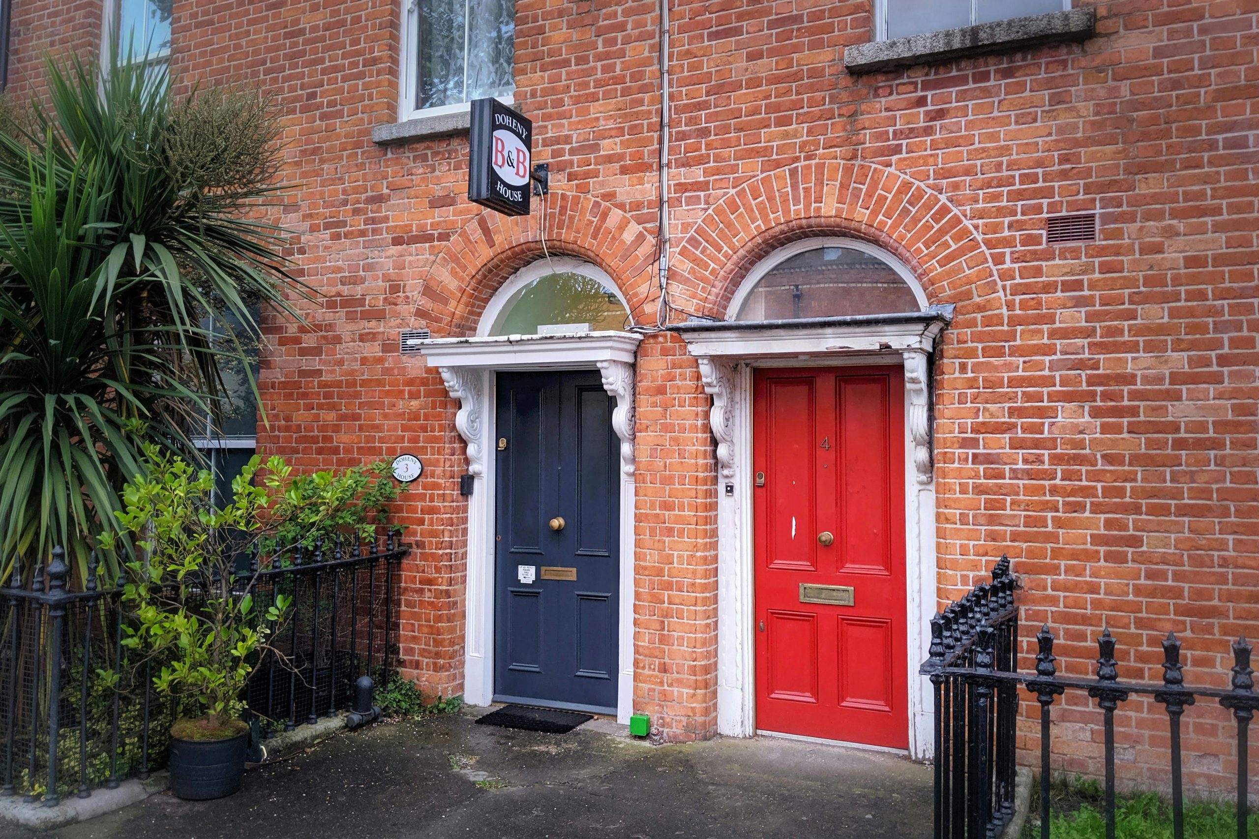 Charming brick townhouse entrance featuring a red door, B&B sign and ornamental ironwork, popular with tourists.