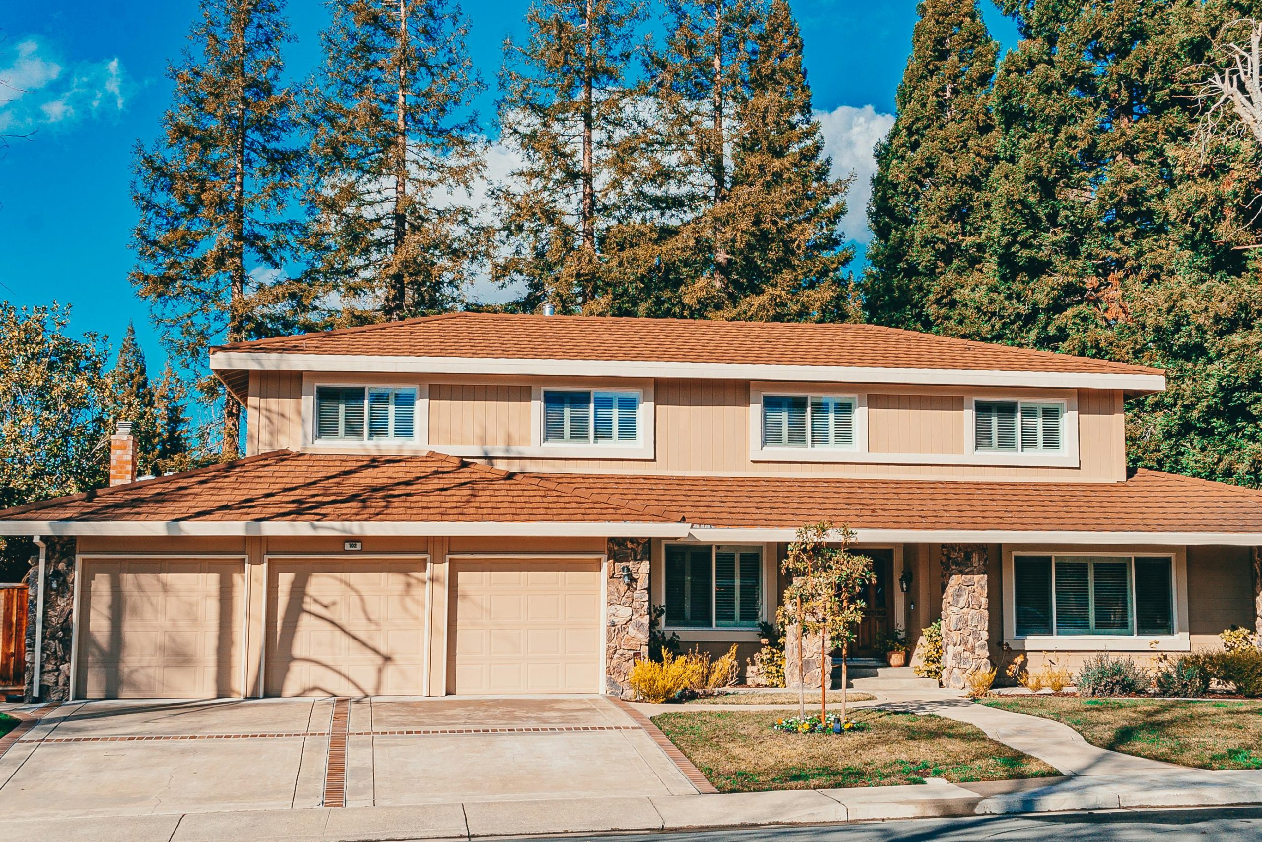 Charming two-story house with a landscaped front yard and wide driveway under clear blue skies.