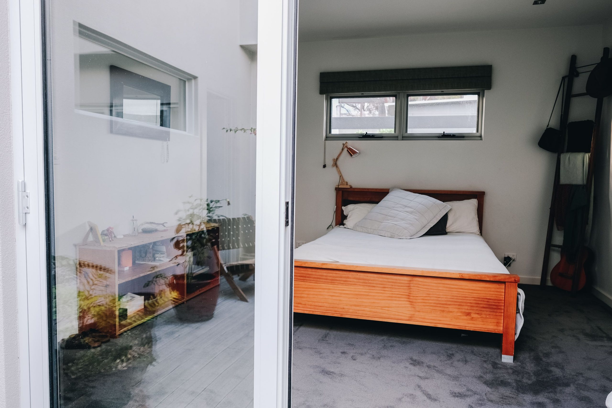 Comfortable bed with pillows placed in light room with wooden furniture and balcony in modern house