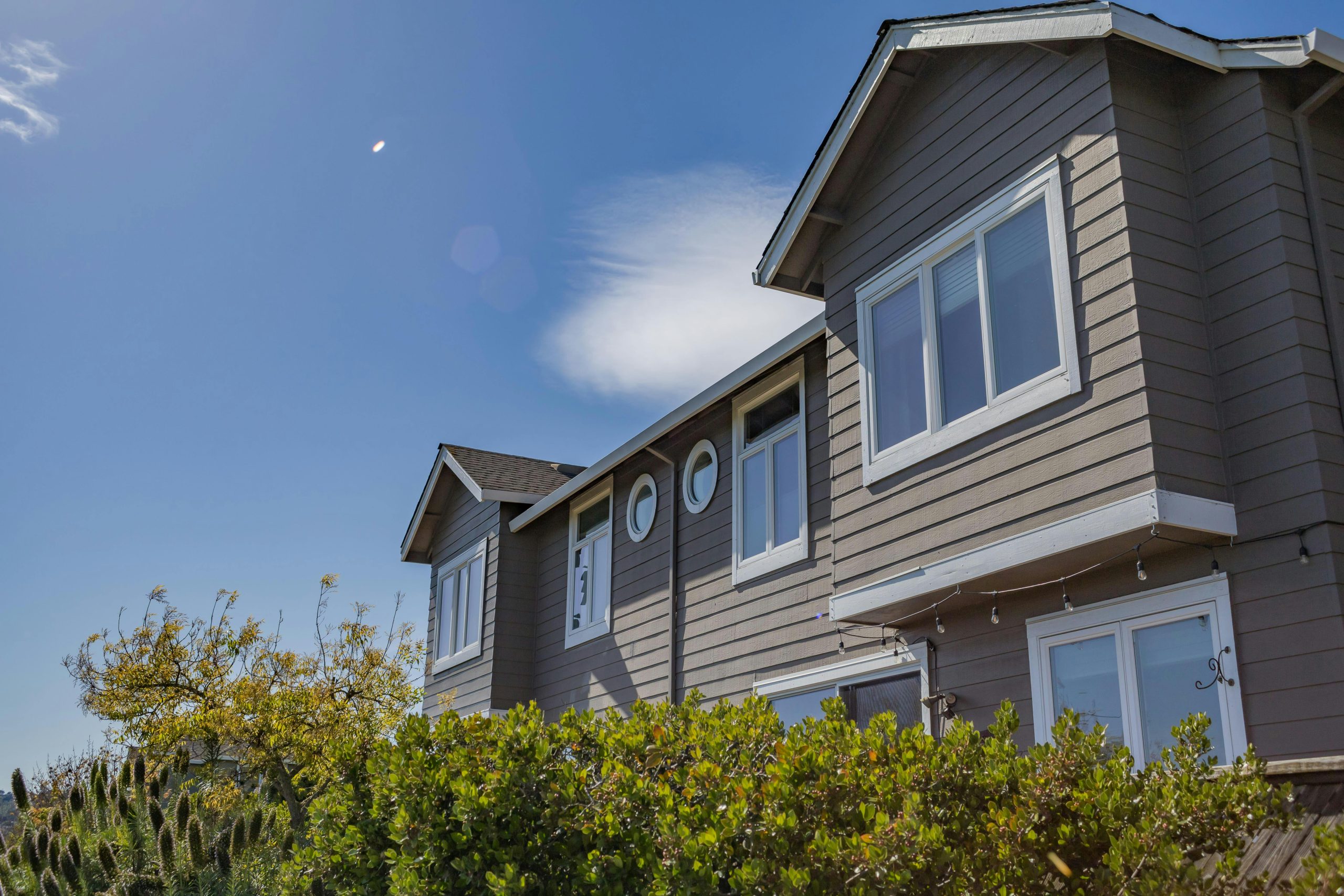 Contemporary suburban house exterior with lush greenery under a clear blue sky.