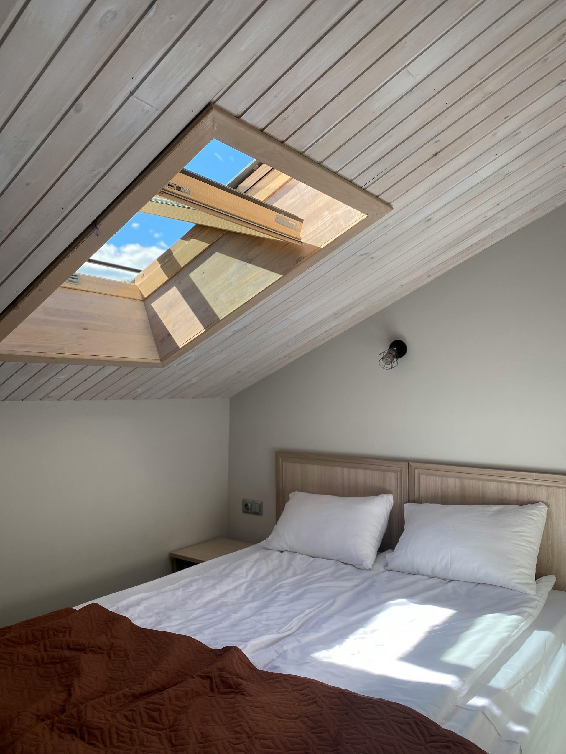 Cozy attic bedroom featuring a skylight with clear sky view and bright sunlight.