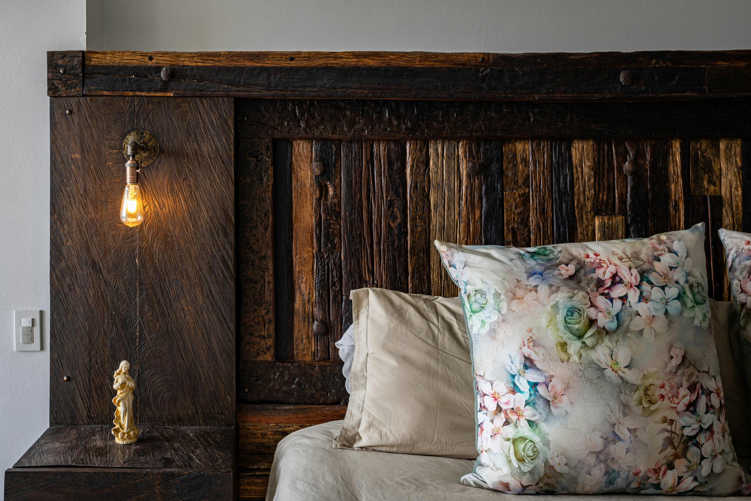 Cozy bedroom corner featuring a rustic wooden headboard and floral pillows in Chía, Colombia.