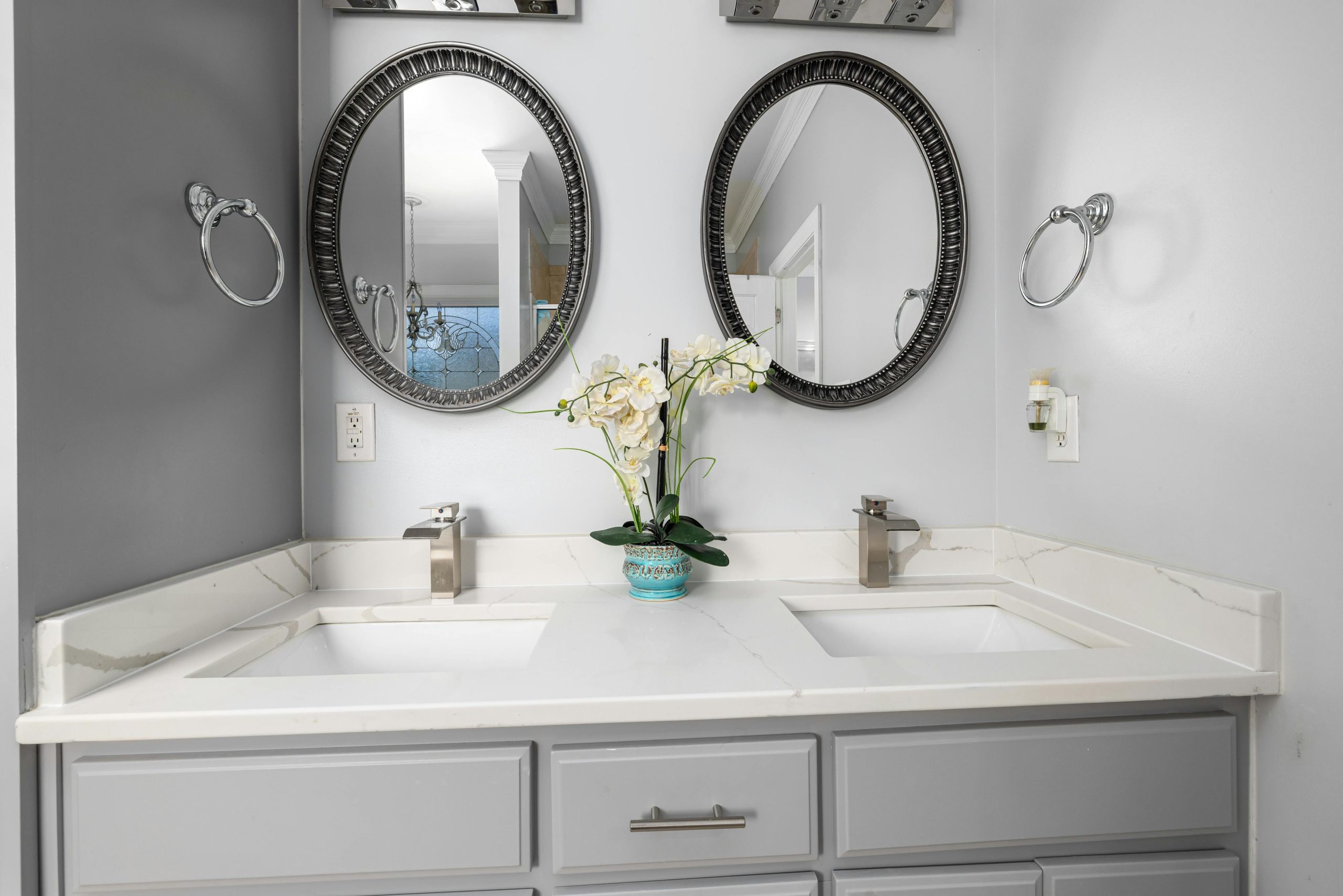 Elegant bathroom with dual sinks, mirrors, and a marble countertop featuring contemporary fixtures.