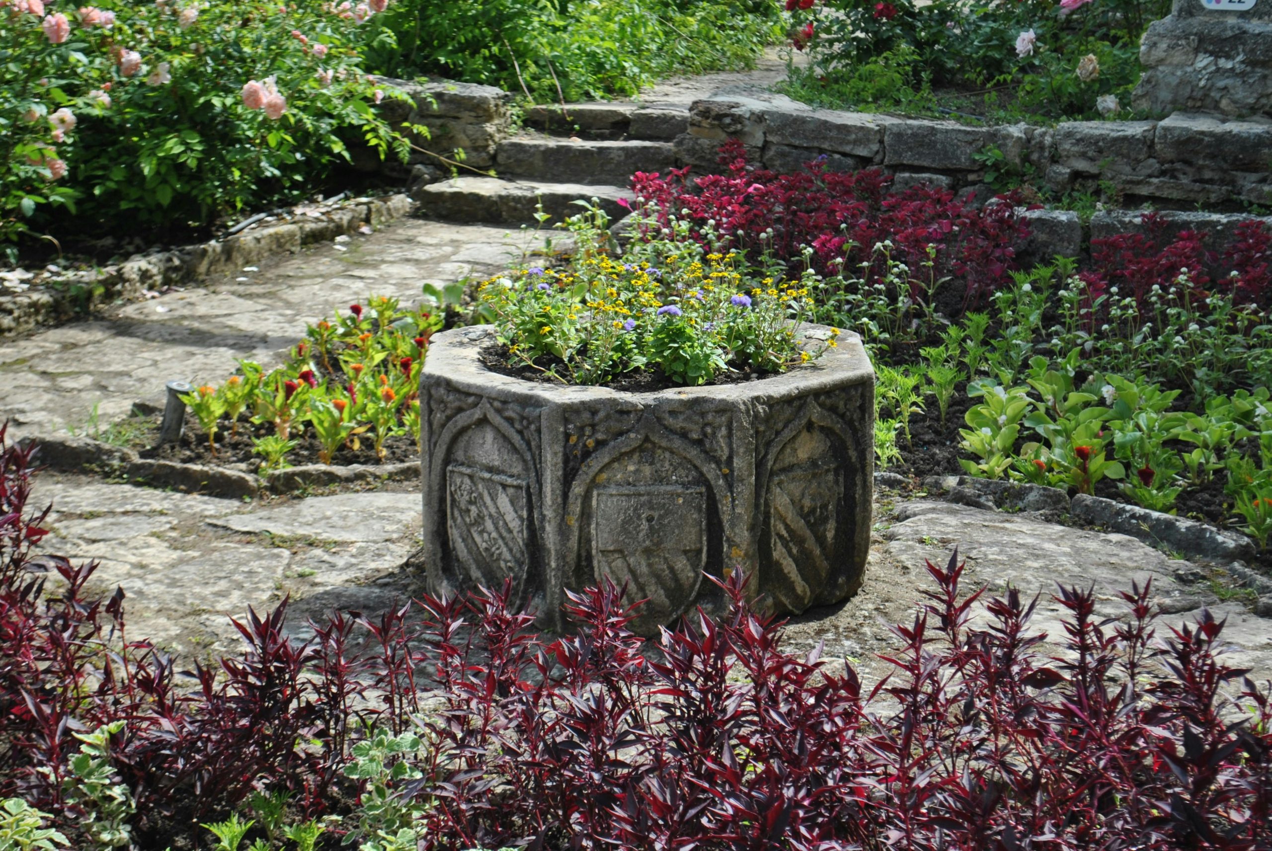 Elegant stone planter amid colorful garden flowers in a historic setting.