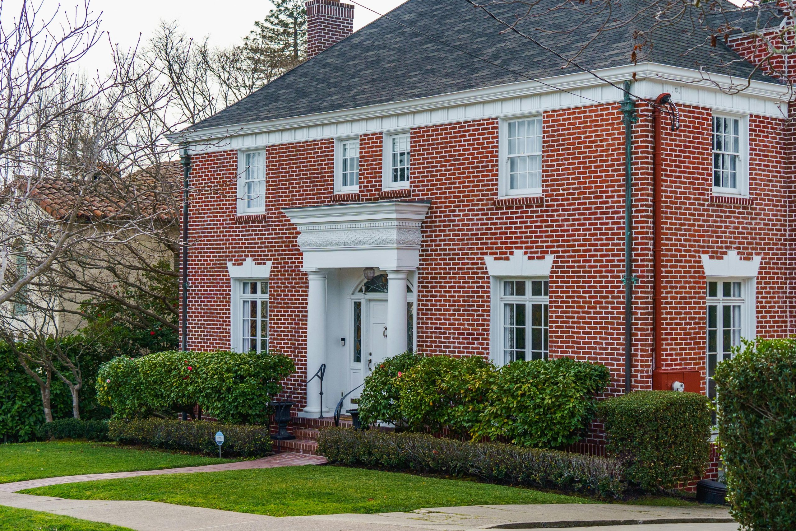 Elegant traditional red brick home with lush garden, showcasing classic American architecture.