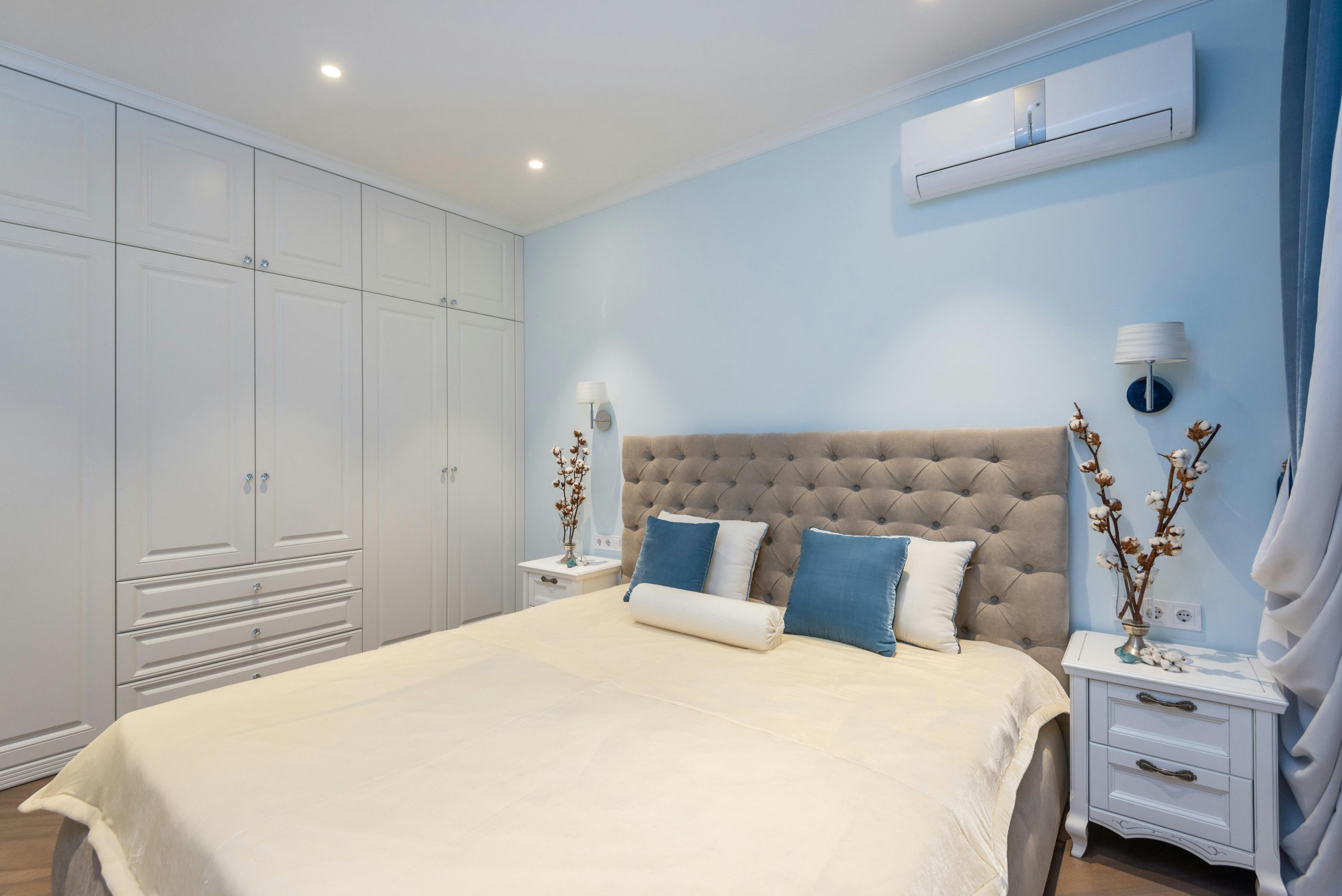 Interior of classic styled bedroom with comfy bed big wardrobe and nightstands decorated with vases with cotton plants