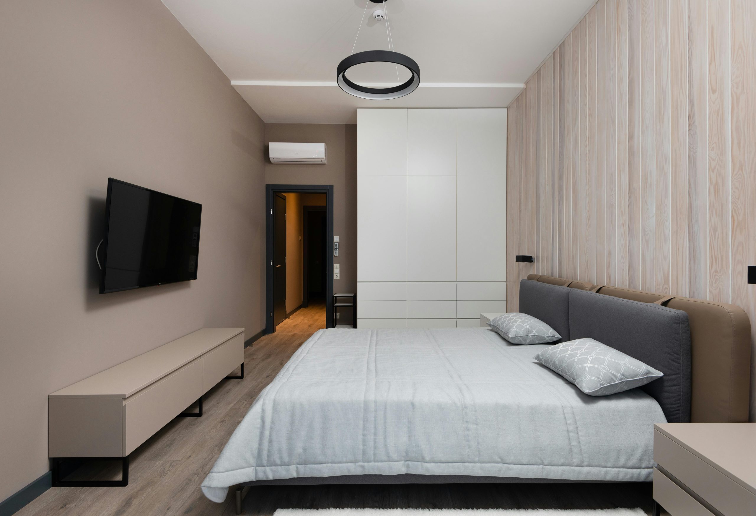 Interior of cozy bedroom with comfortable bed with pillows modern TV set and wardrobe