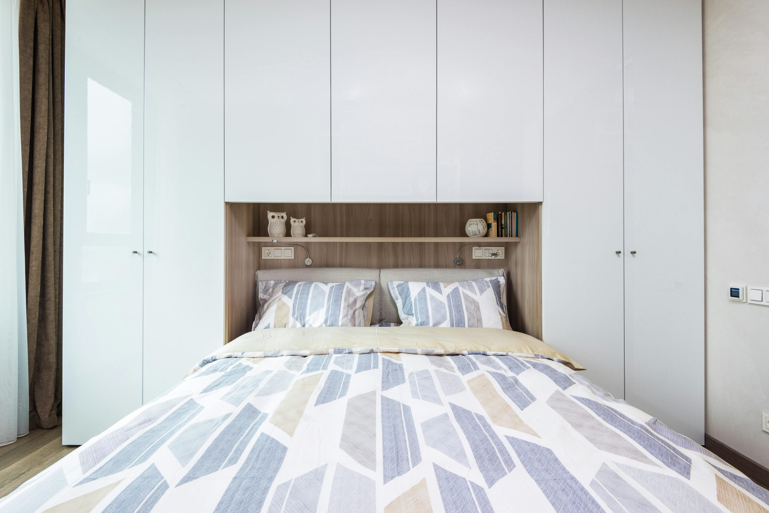 Interior of modern comfortable bedroom with bed with pillows and blanket under shelf combined with bedside wardrobe