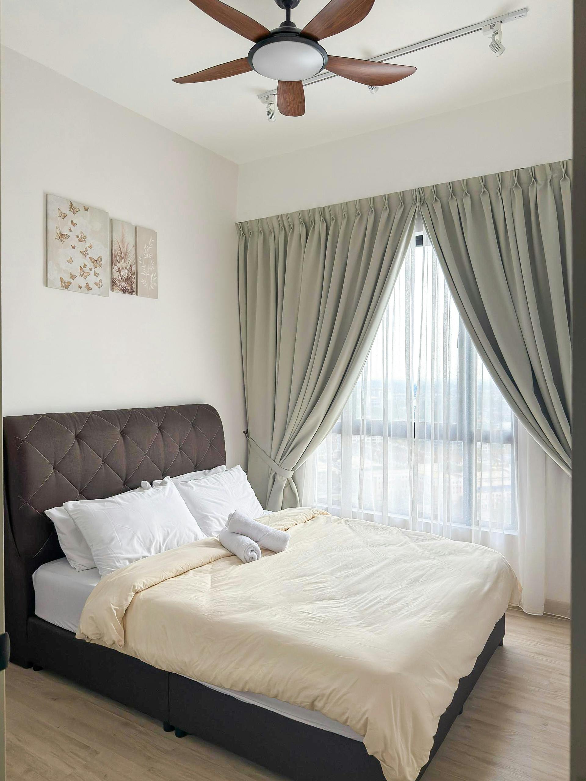 Modern bedroom in Ipoh with brown bed, beige duvet, and natural light through large window.