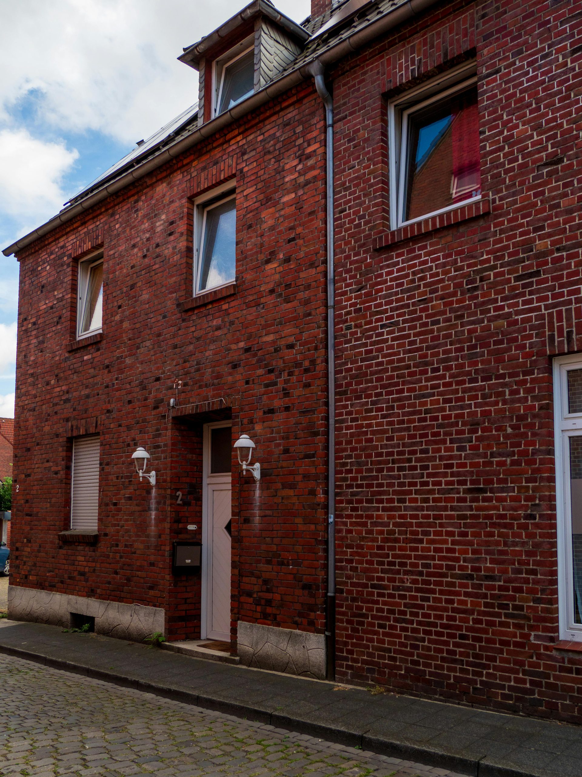 Red brick house with classic architecture on a peaceful street under a blue sky.