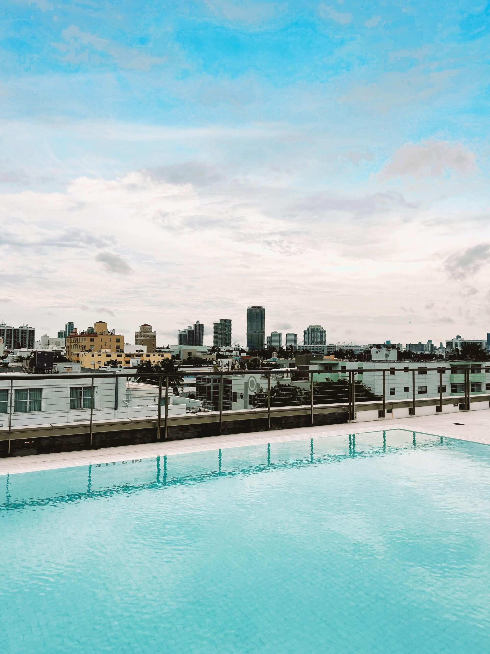 Rooftop pool overlooking a vibrant city skyline under a bright blue sky.