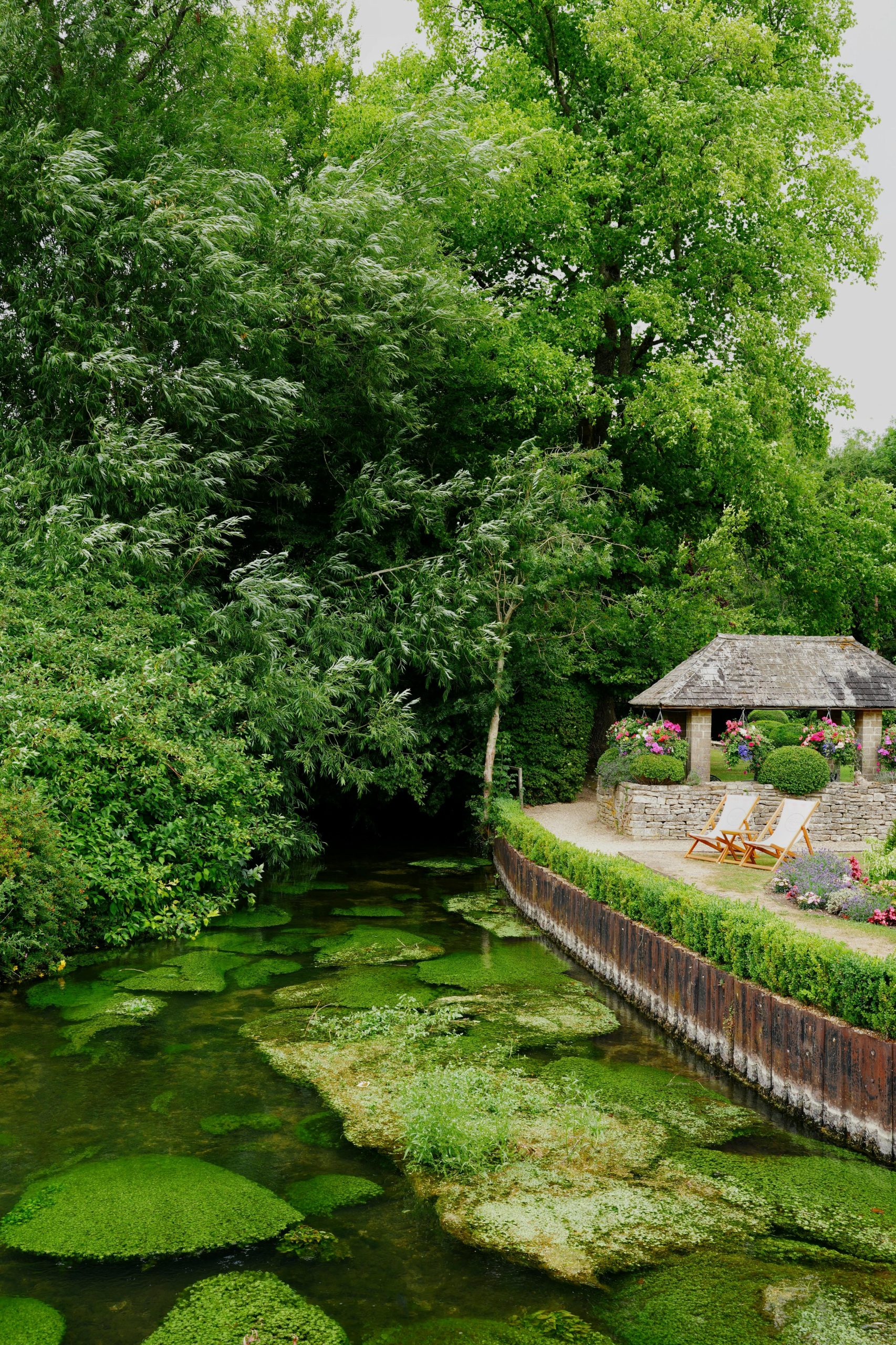 Scenic view of a traditional stone cottage beside a vibrant green stream in a rural English setting.