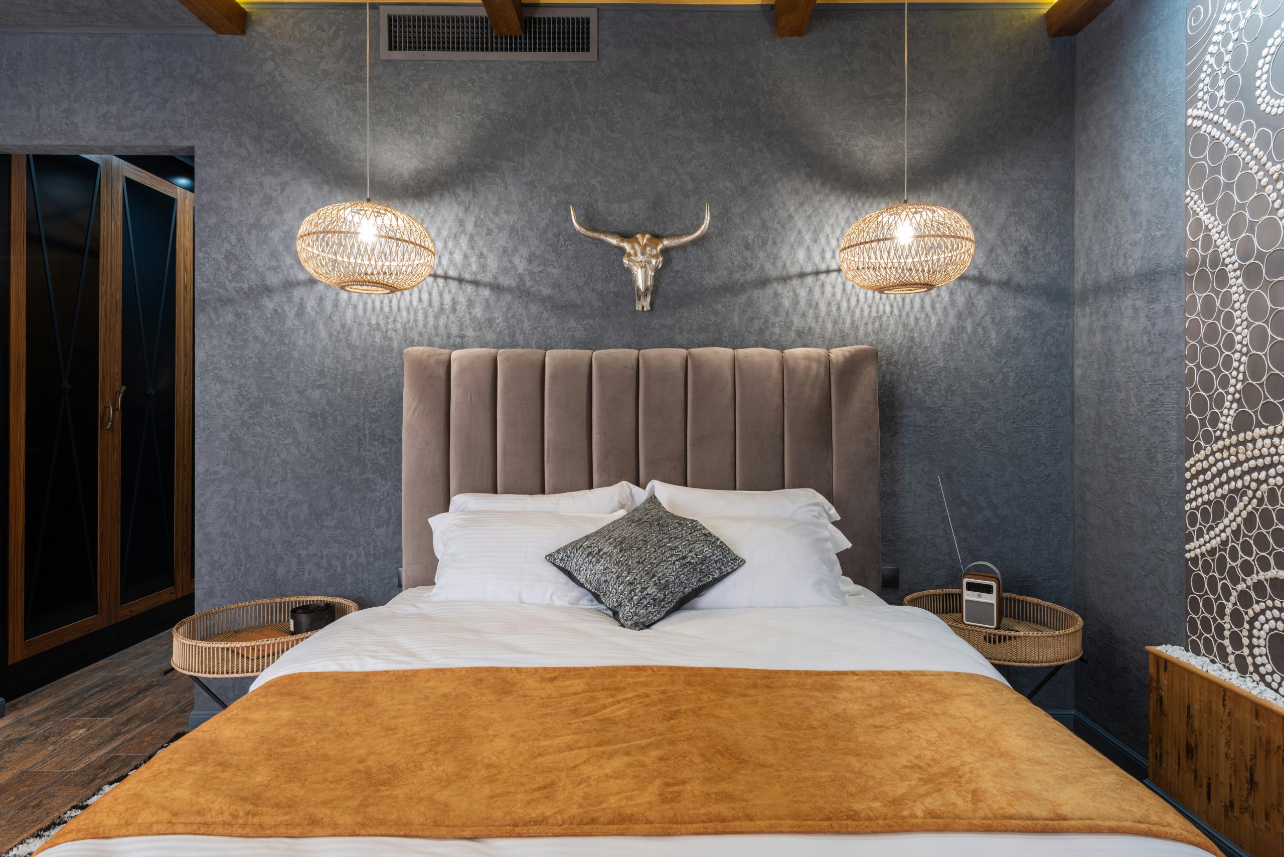 Soft bed with cover and pillows between glowing lamps and oriental panel in hotel room