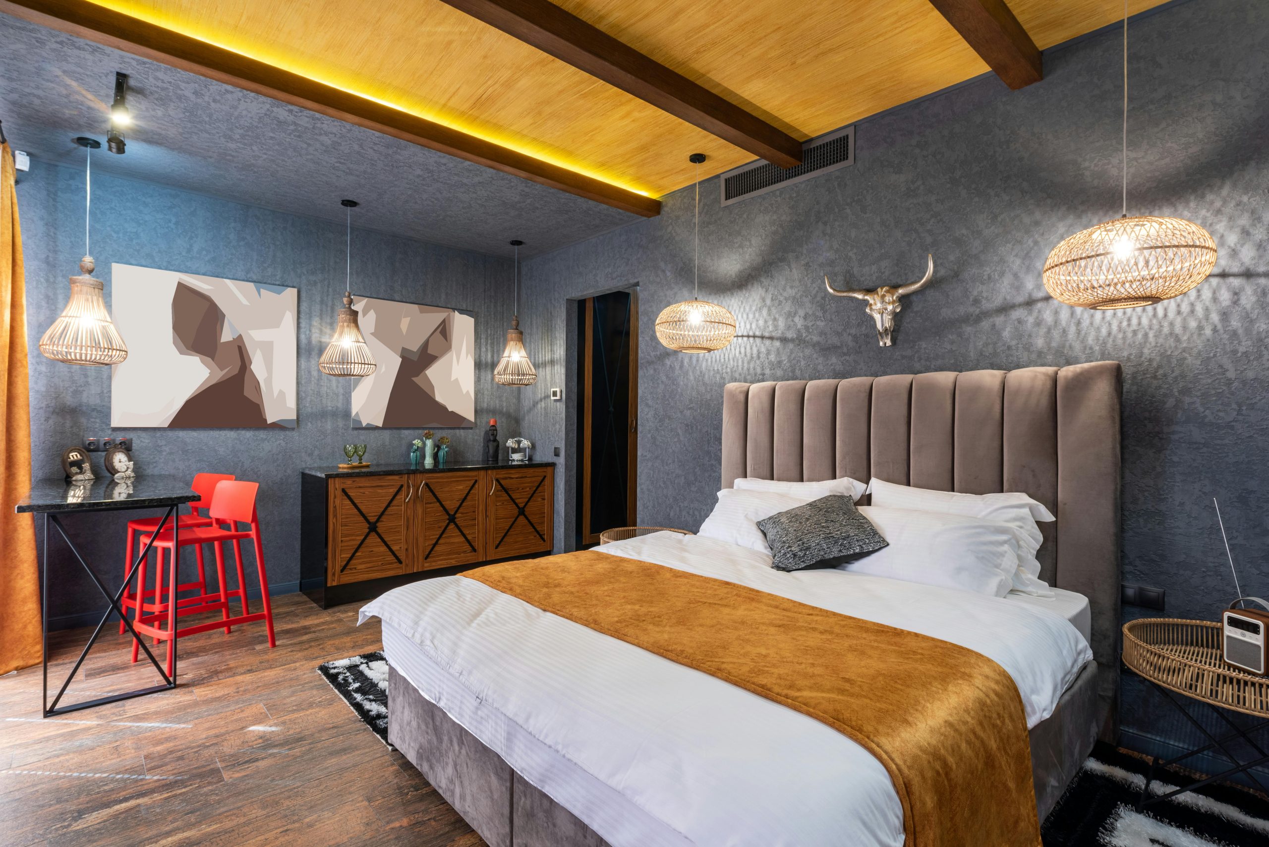 Soft bed with pillows under decorative deer horns and glowing lights in house with paintings on wall